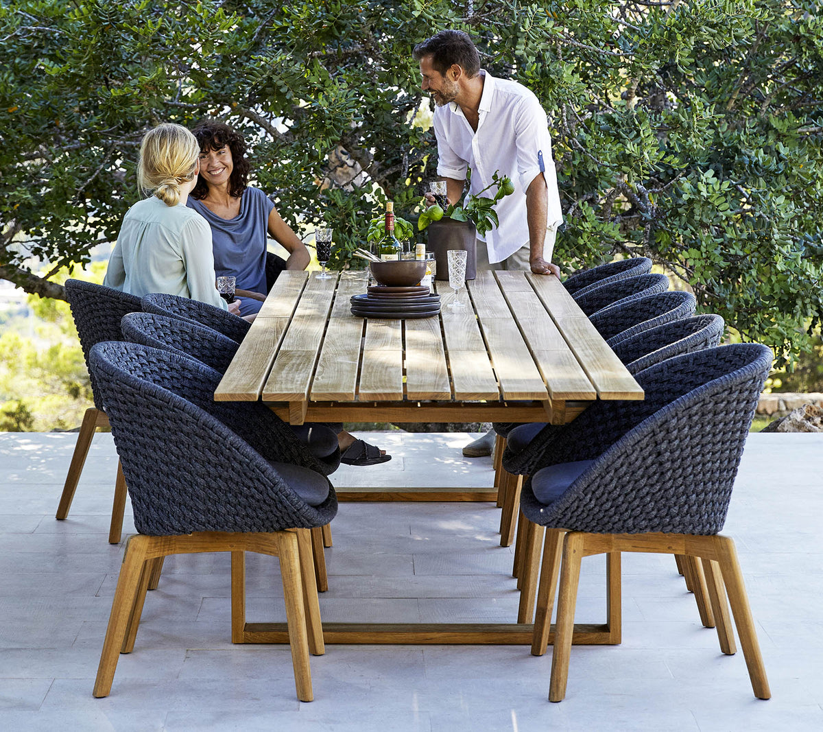 Une disposition de salle à manger élégante avec une table en bois entourée de chaises confortables, avec trois personnes engagées dans une conversation, au milieu de la verdure.