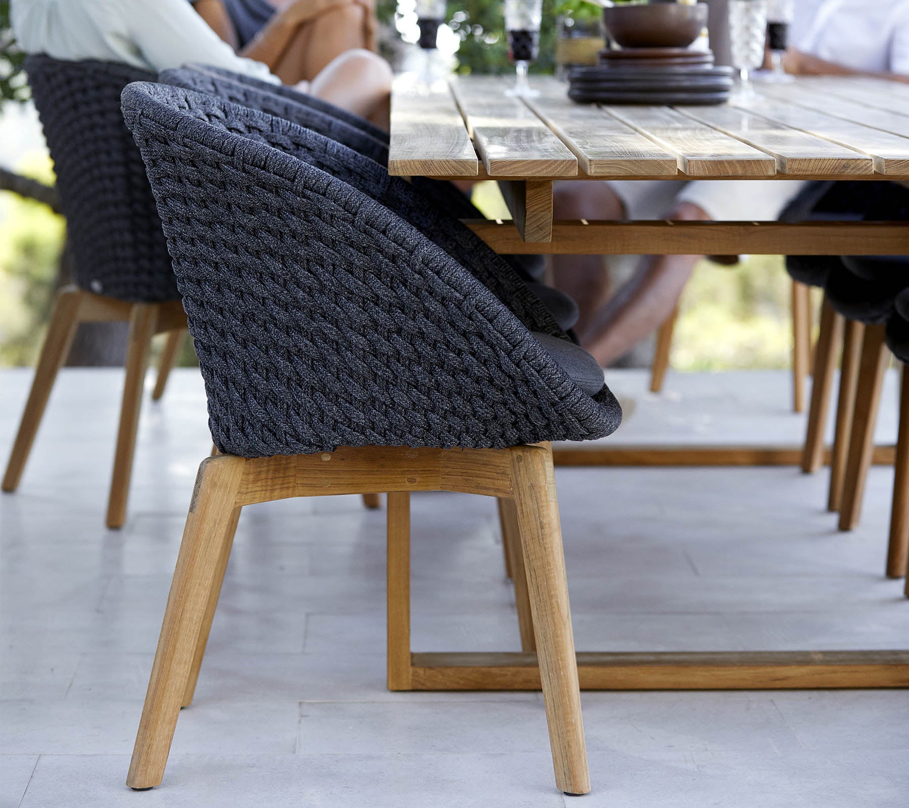 Une chaise élégante avec un dossier tissé et des pieds en bois, placée à côté d'une table à manger en bois, avec des personnes engagées à proximité.