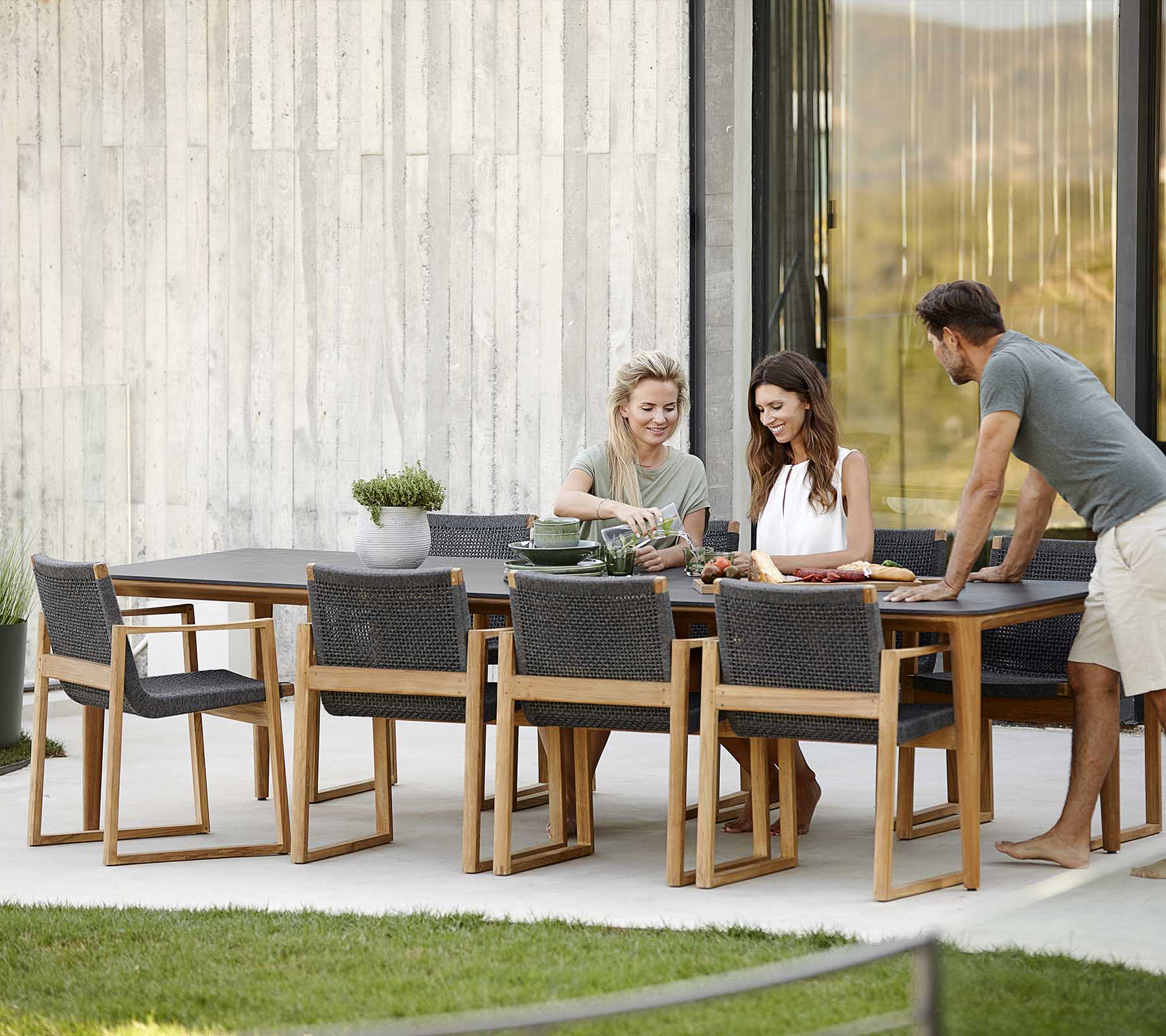 Quatre personnes partagent un repas ensemble autour d'une table en bois élégante, avec des chaises modernes et un cadre extérieur serein.