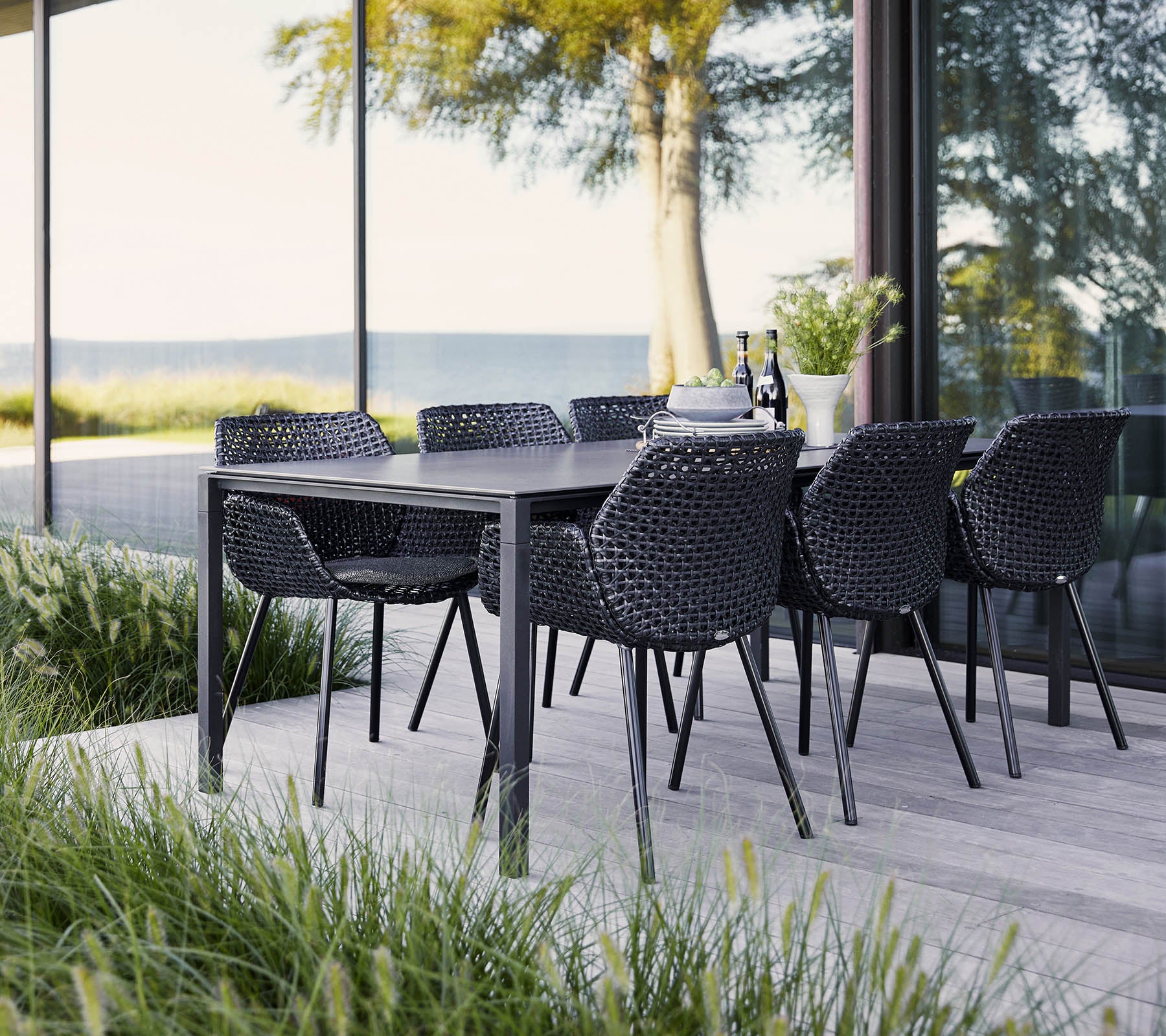Un ensemble de repas élégant avec une table noire et des chaises tressées, entouré d'une végétation luxuriante et de vues panoramiques. Idéal pour les rassemblements.