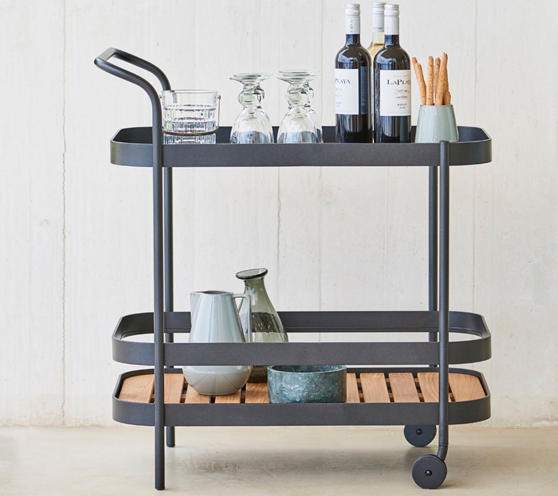 Un chariot à boissons élégant avec des verres, des bouteilles de vin et des ustensiles sur trois niveaux, avec un cadre en métal sleek et des accents en bois.