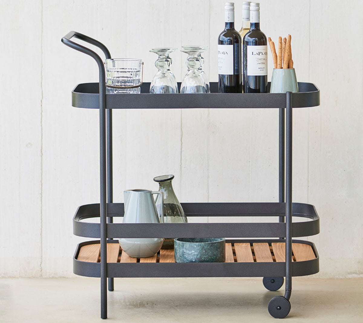 Un chariot à boissons élégant avec des verres, des bouteilles de vin et des ustensiles sur trois niveaux, avec un cadre en métal sleek et des accents en bois.