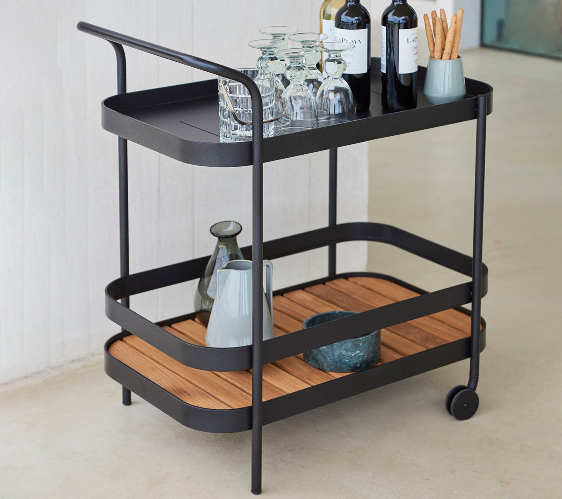 Chariot de service élégant à deux niveaux, avec de la verrerie, des bouteilles de vin et un vase, avec un mélange d'éléments de design en métal et en bois.