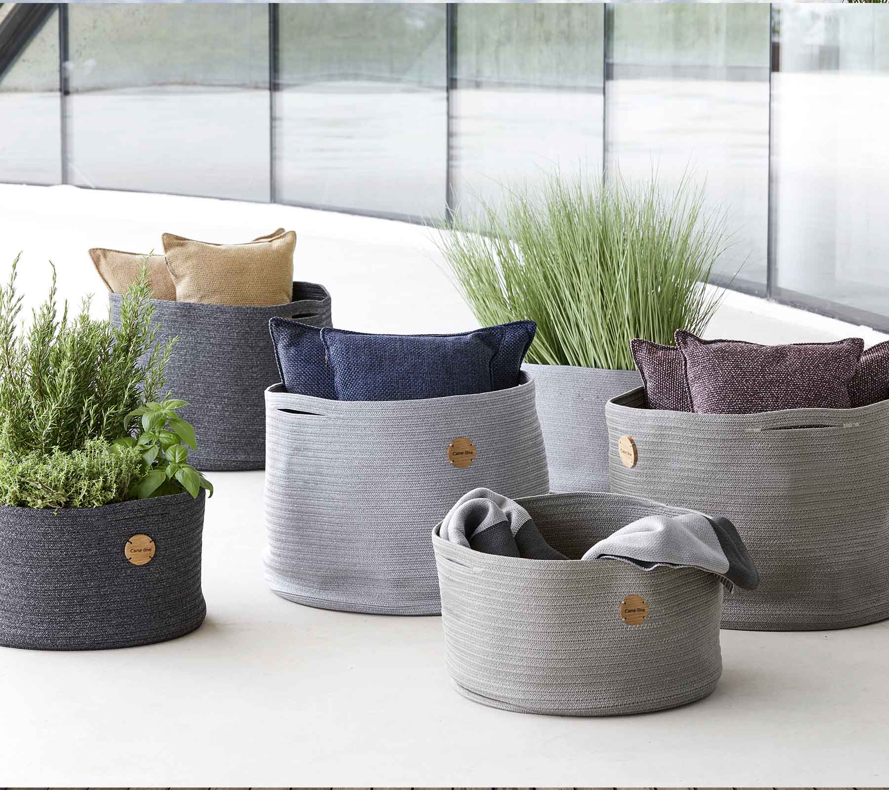 Une variété de paniers de rangement tissés élégants de différentes tailles, avec des coussins vibrants et de la verdure pour une touche décorative.