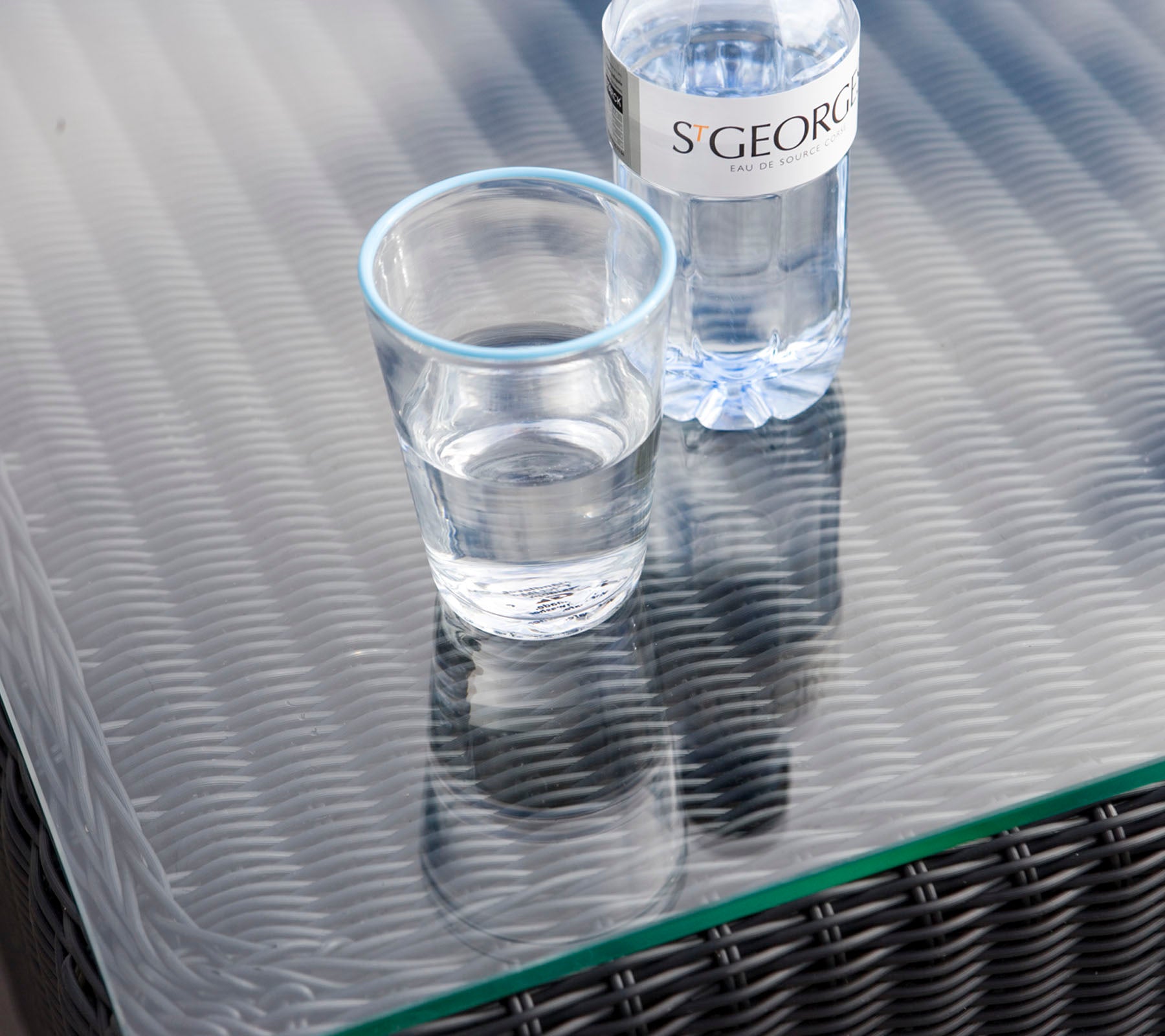 Un verre clair avec de l'eau à côté d'une bouteille d'eau sur une surface de table texturée.