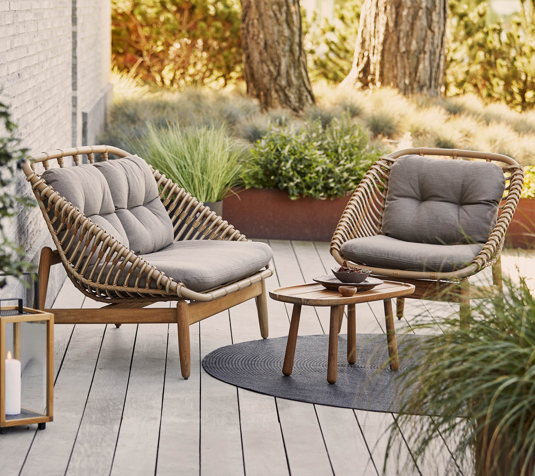 Deux chaises élégantes avec des coussins moelleux entourent une petite table en bois sur une surface texturée, complétée par des plantes vertes en arrière-plan.