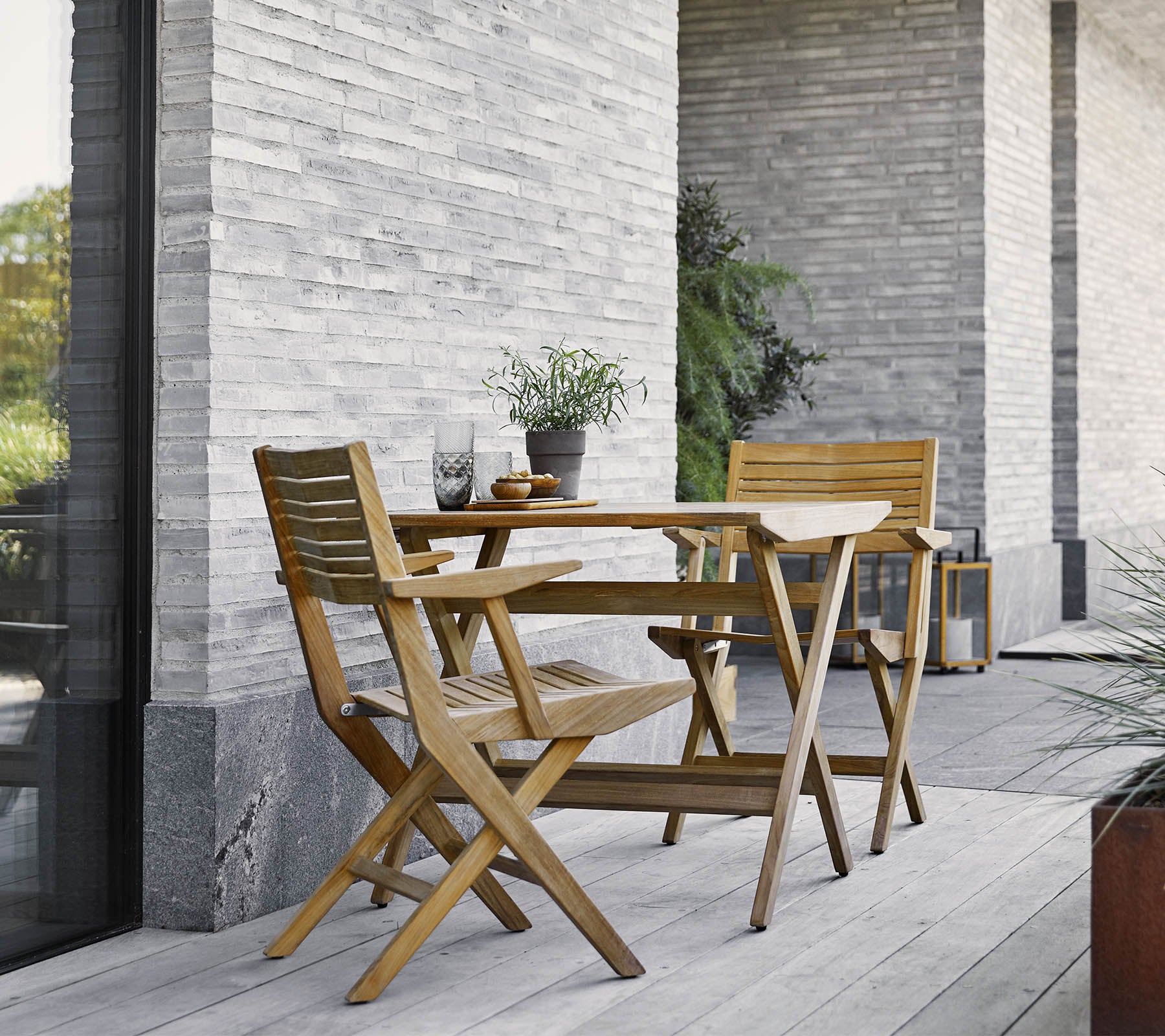 Une table pliante en bois avec deux chaises assorties, ornée de plantes en pot, contre un mur en pierre texturé.