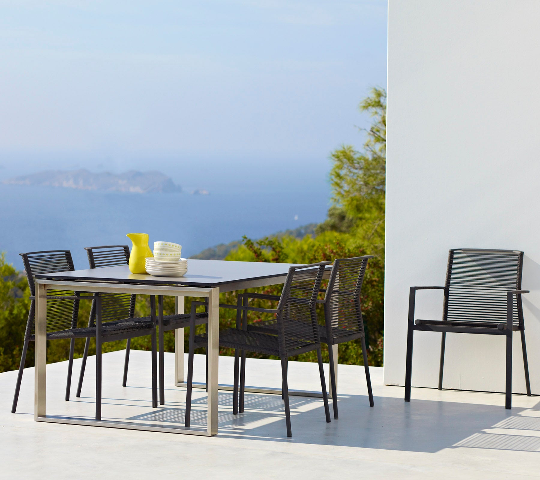 Un ensemble de salle à manger élégant comprenant une table rectangulaire, six chaises et un vase avec des fleurs jaunes, sur fond de paysage pittoresque.