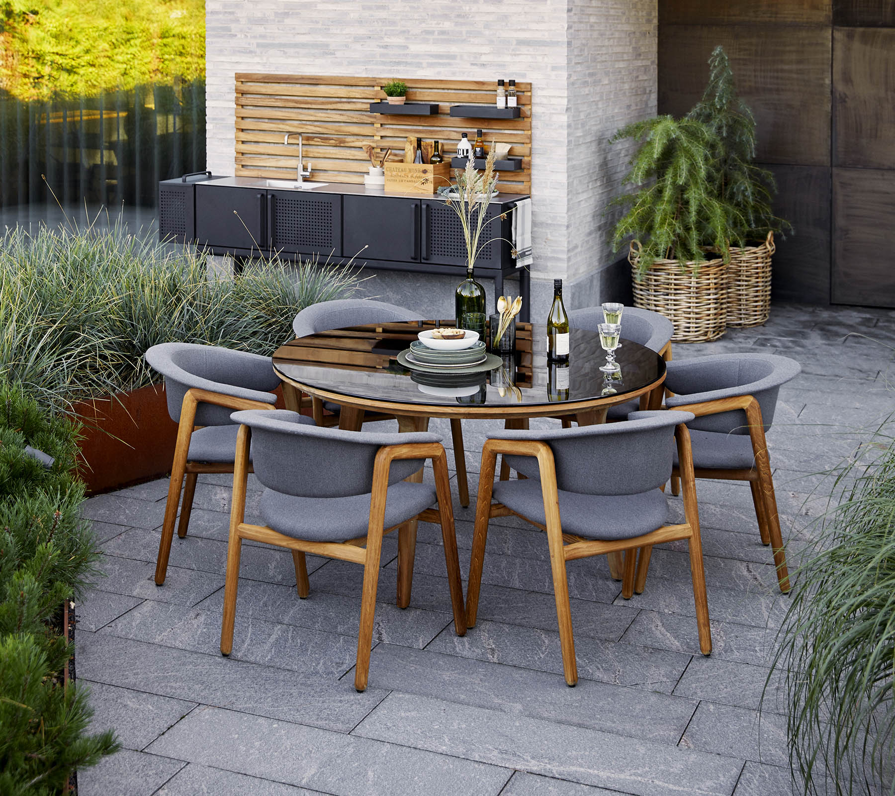Un ensemble de table à manger rond moderne avec des chaises grises, présentant des éléments décoratifs et une verdure en arrière-plan.