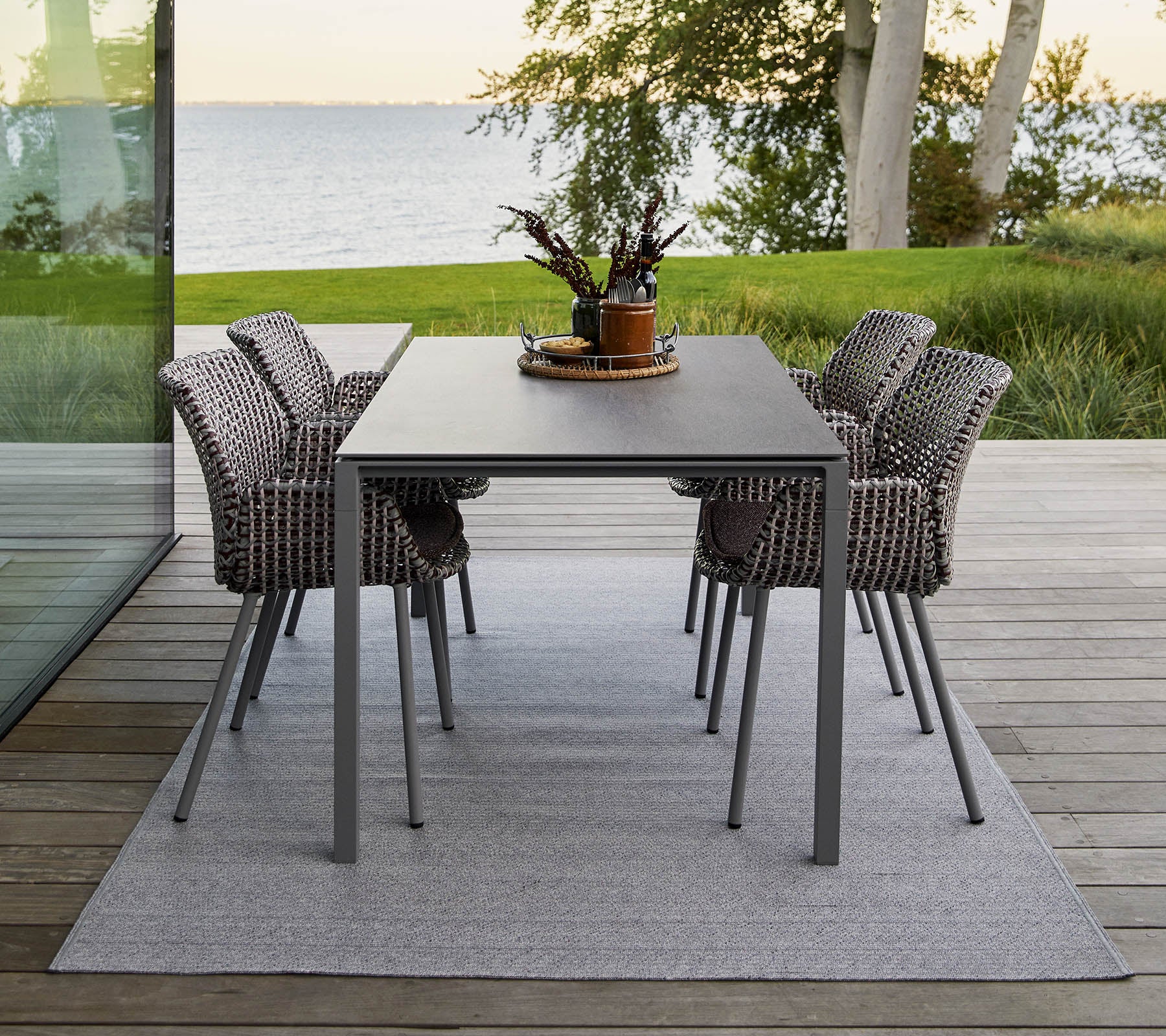 Une table à manger moderne avec quatre chaises tissées élégantes, ornée d'un centre de table décoratif en plante sur un tapis doux.
