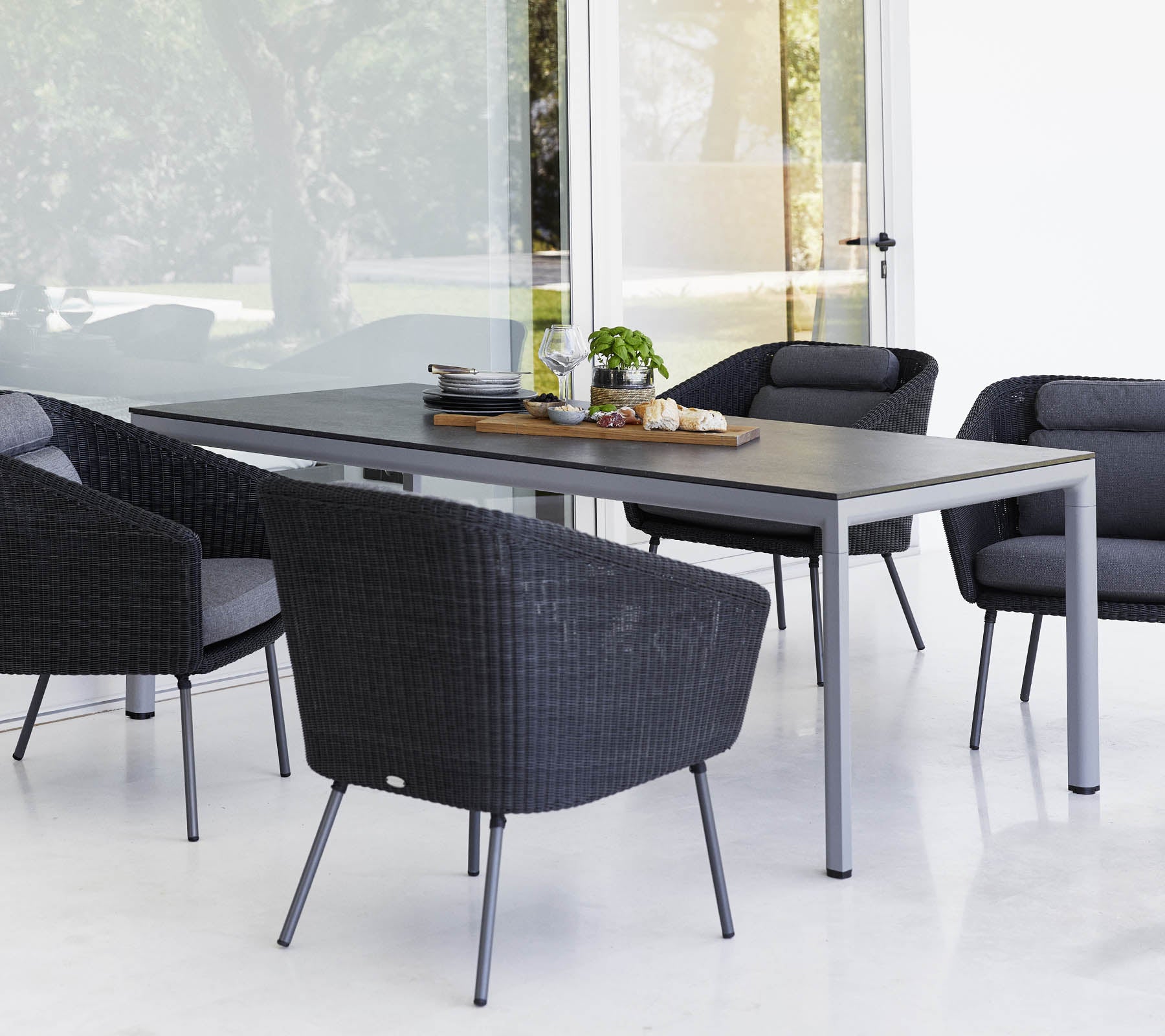 Une table à manger moderne entourée de quatre chaises de jardin noires élégantes, avec un centre de table et de la verdure sur la table.