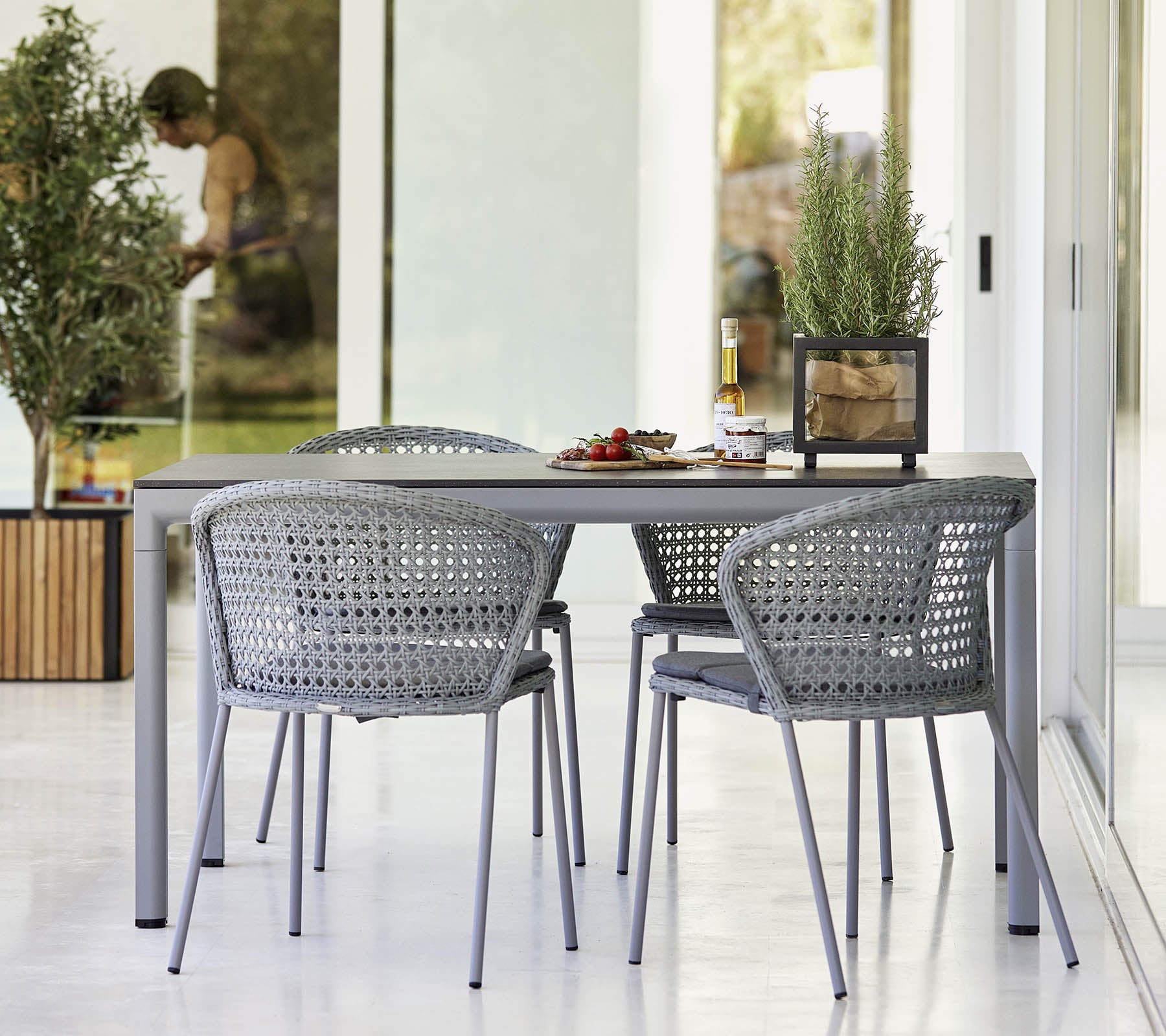 Ensemble de salle à manger moderne avec une table épurée et des chaises tressées, complété par de la verdure et une atmosphère légère et aérée.