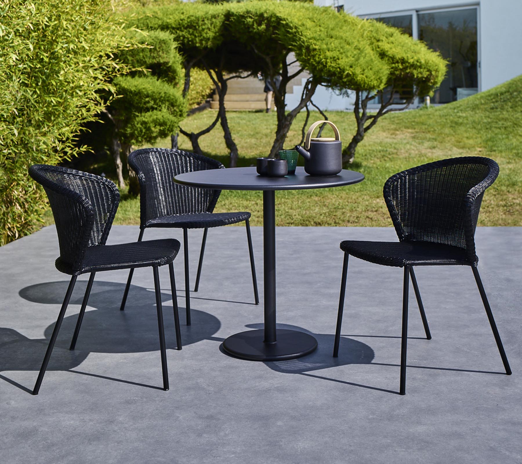 Un ensemble de table d'extérieur moderne avec une table ronde et trois chaises tressées noires, entièrement équipé d'une théière et de tasses sur la table.