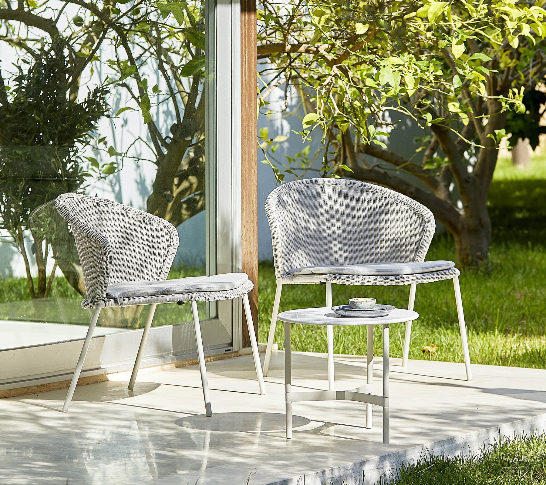 Deux chaises élégantes et une petite table dans un cadre serein avec de la verdure, parfait pour se détendre et pour des rassemblements en plein air.