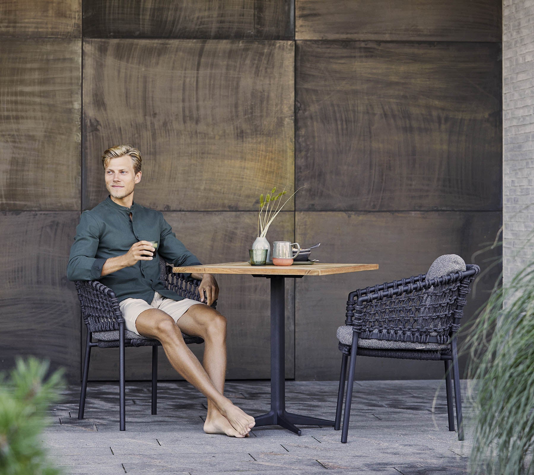 Une personne est assise détendue à une table, profitant d'une boisson, entourée de chaises en osier élégantes et d'éléments décoratifs.