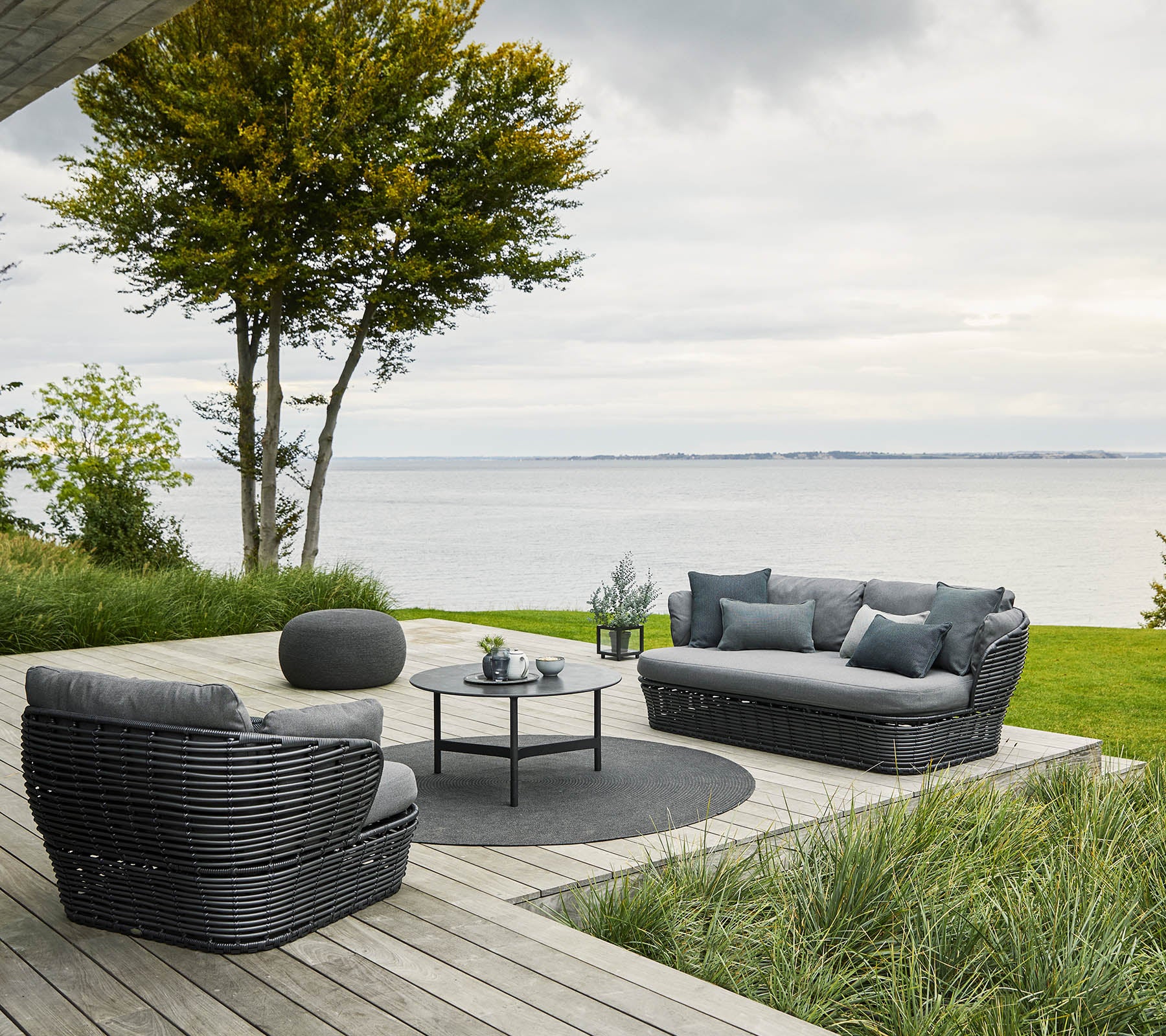 Agencement confortable avec un canapé et des chaises disposés autour d'une table ronde, entouré de verdure et d'une vue sur l'eau.