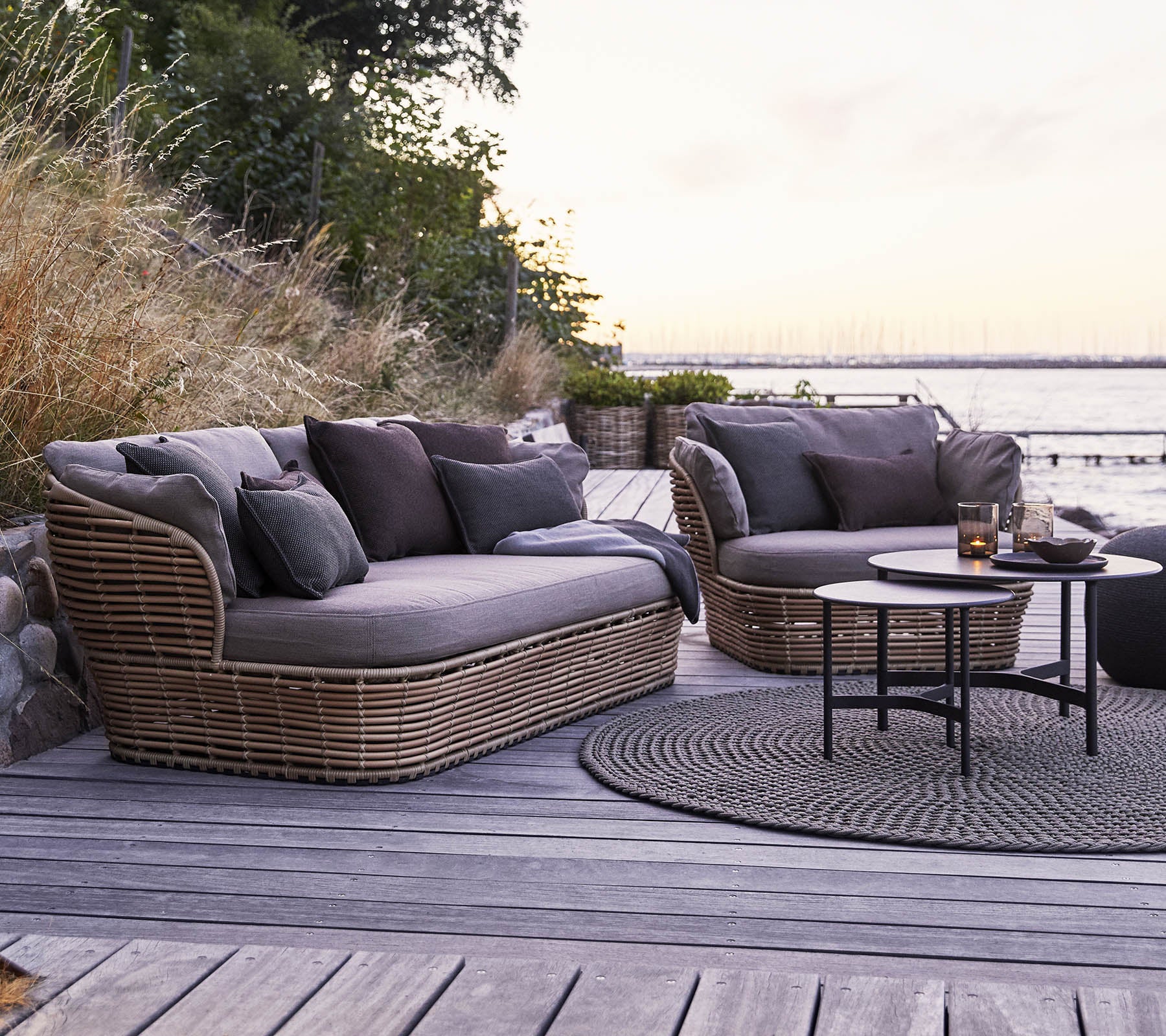Espace extérieur élégant avec deux canapés courbés et moelleux avec des coussins sombres et une table basse ronde sur une surface en bois.