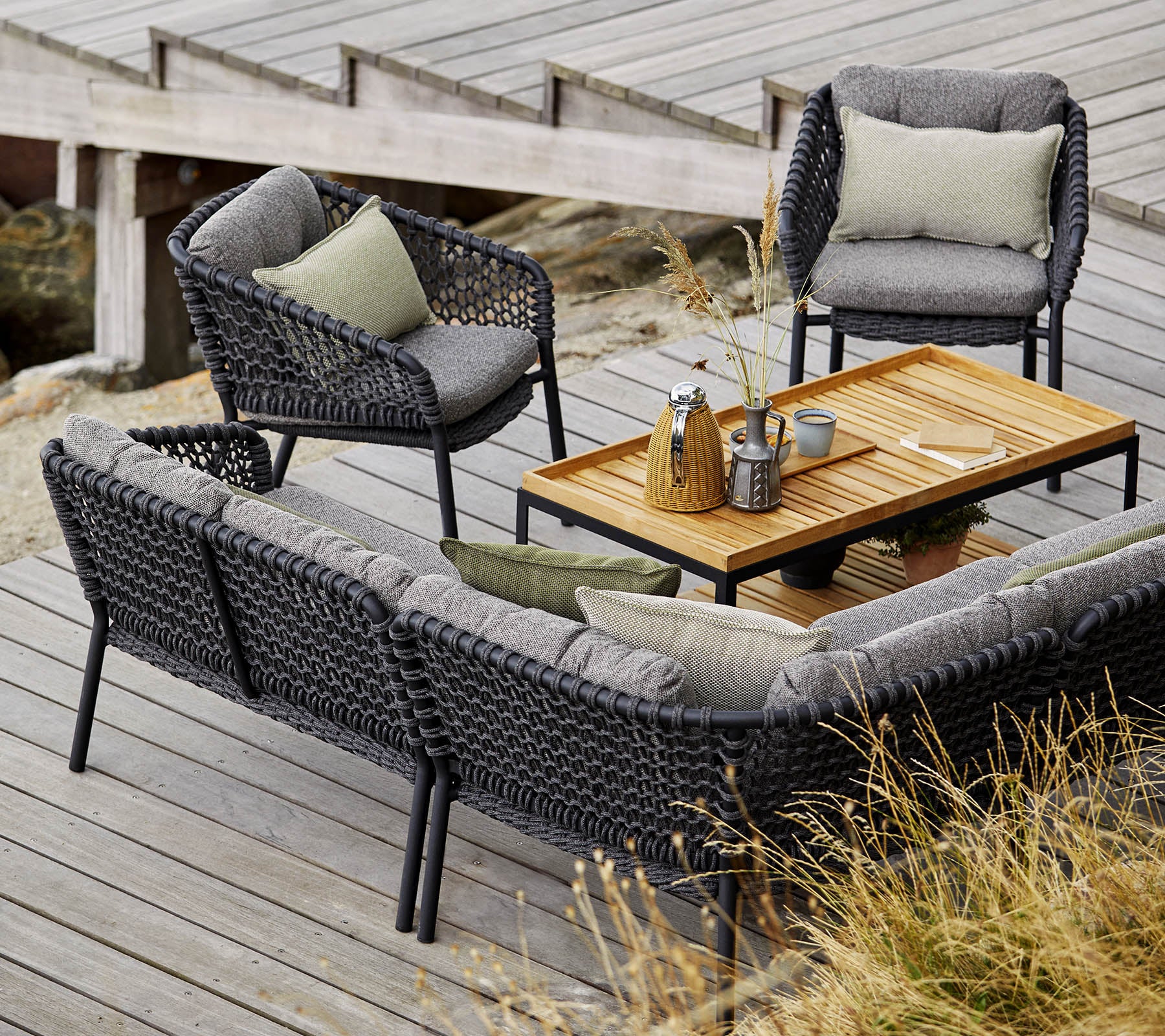 Ensemble de sièges d'extérieur élégant comprenant un canapé confortable, deux chaises et une table basse en bois, rehaussé de coussins doux et d'objets décoratifs.