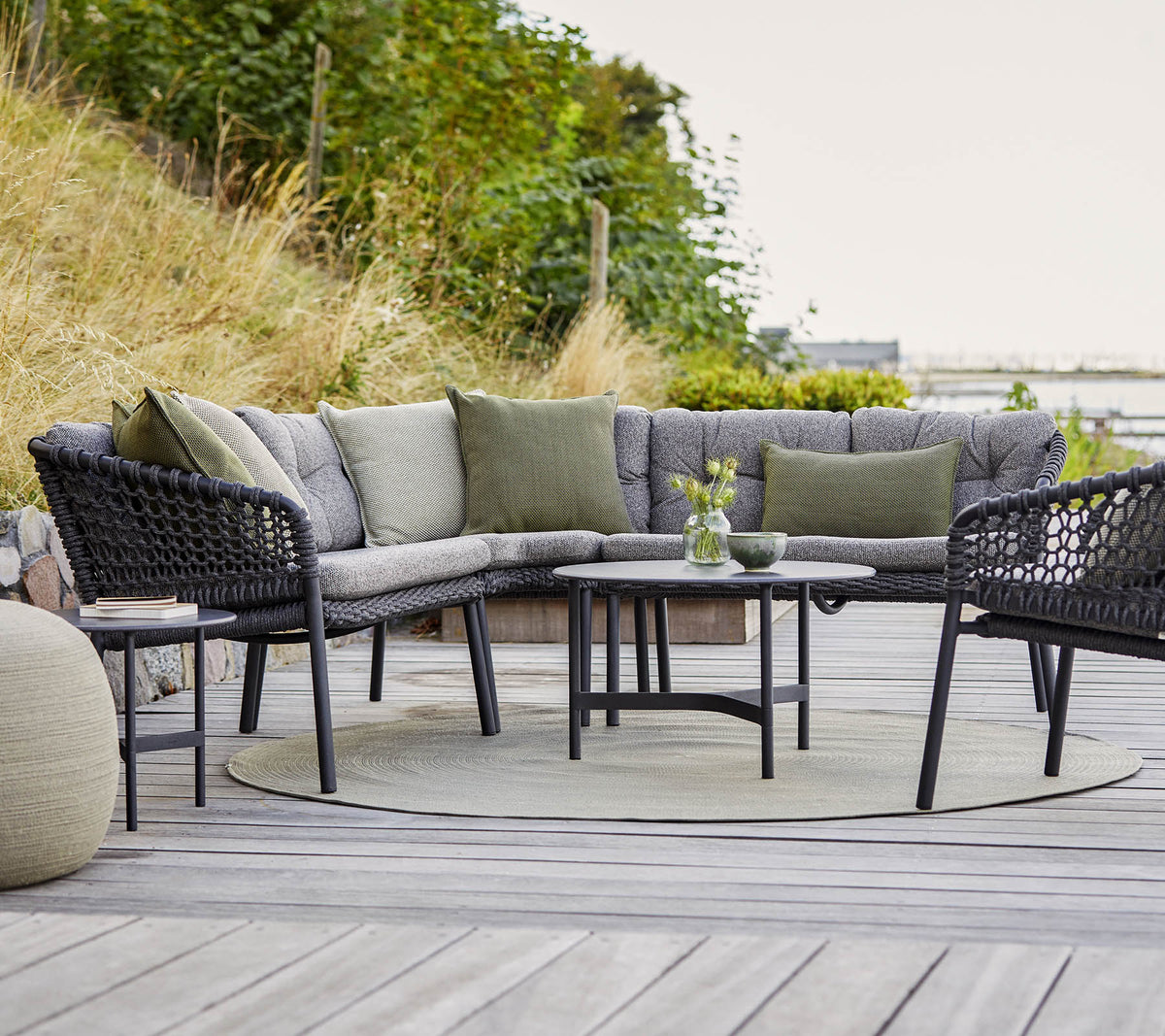 Agencement extérieur élégant comprenant un canapé sectionnel incurvé, une table ronde et des accents confortables dans un cadre naturel.