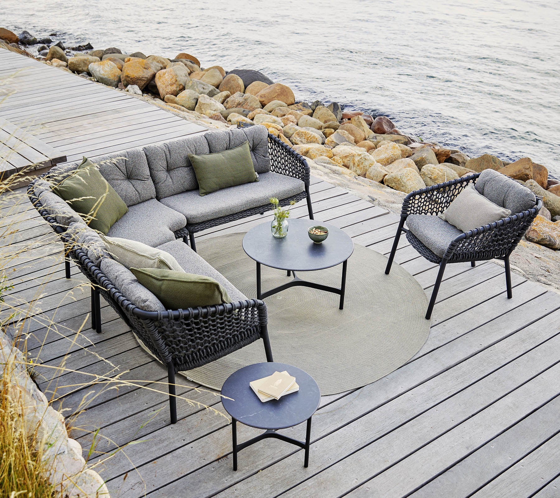 Un agencement extérieur élégant avec un canapé sectionnel et des chaises avec des coussins gris, une table ronde et des accents décoratifs.