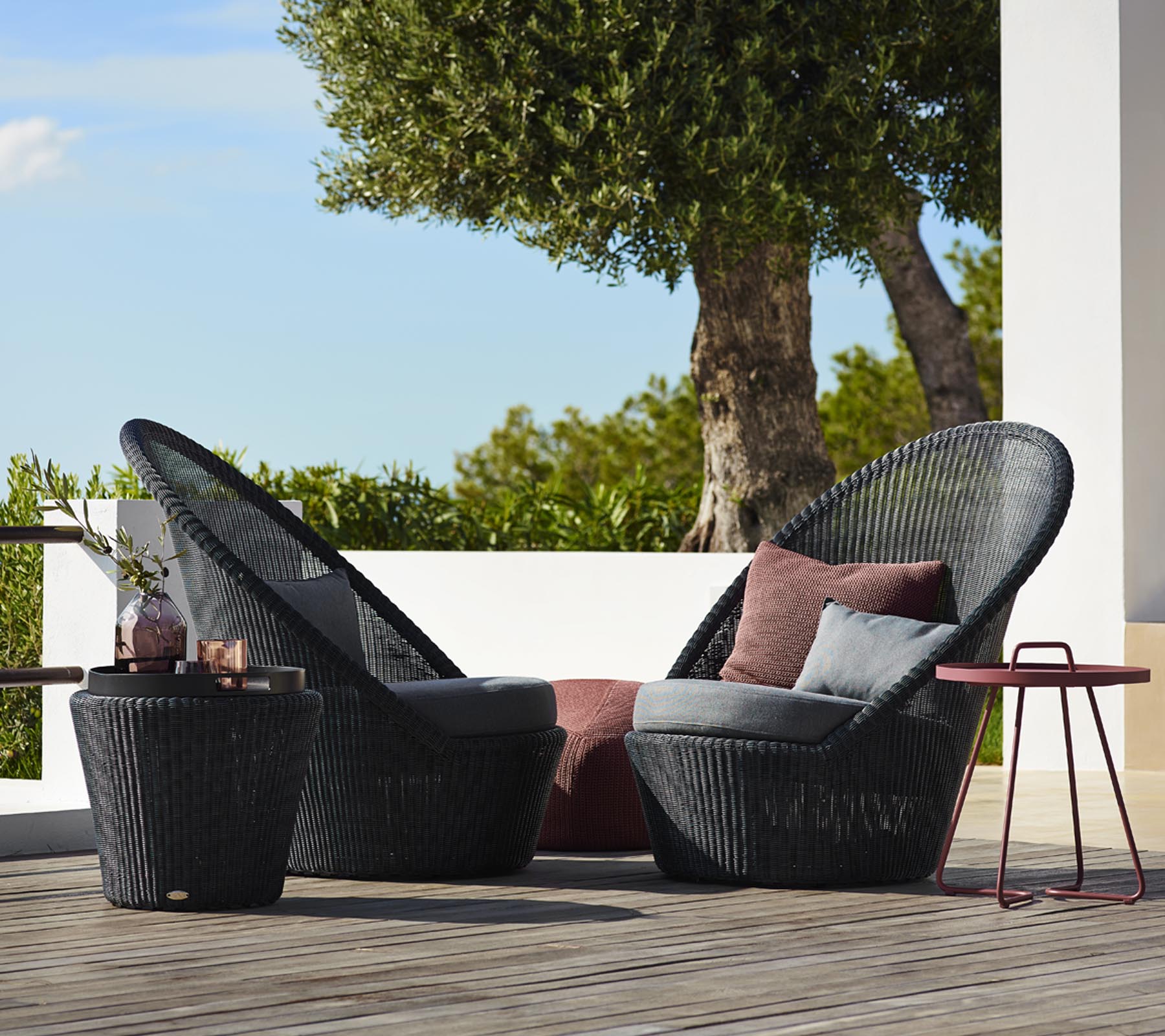 Deux chaises tressées noires élégantes avec des coussins moelleux, accompagnées d'une petite table assortie, sur fond naturel.