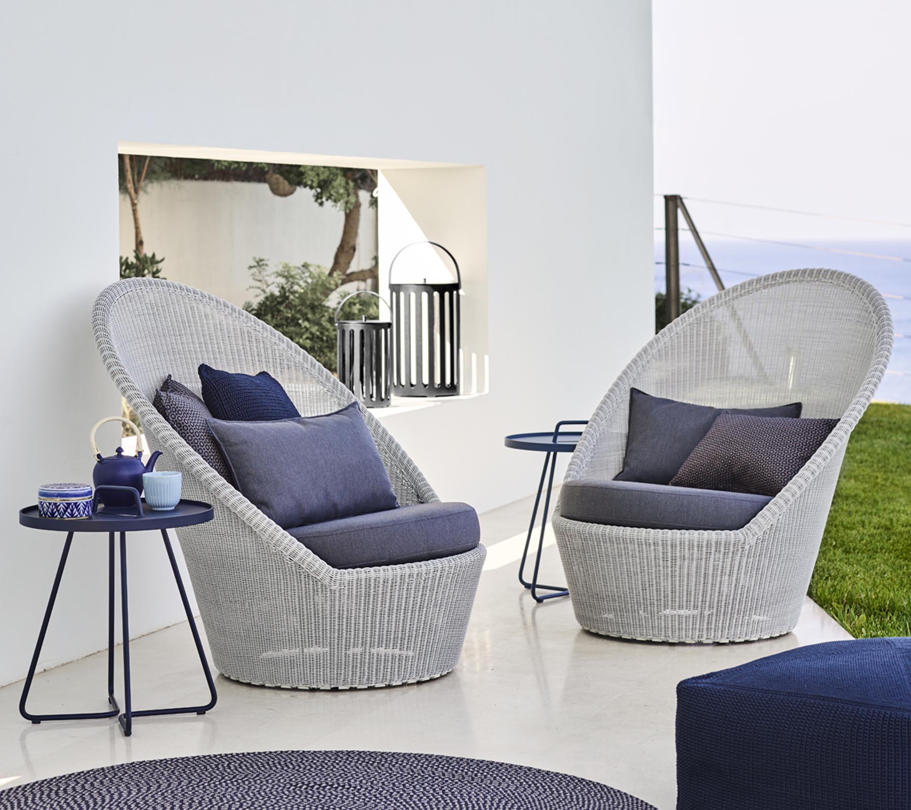 Deux chaises longues tressées élégantes avec des coussins bleus à côté d'une petite table, dans un cadre serein.