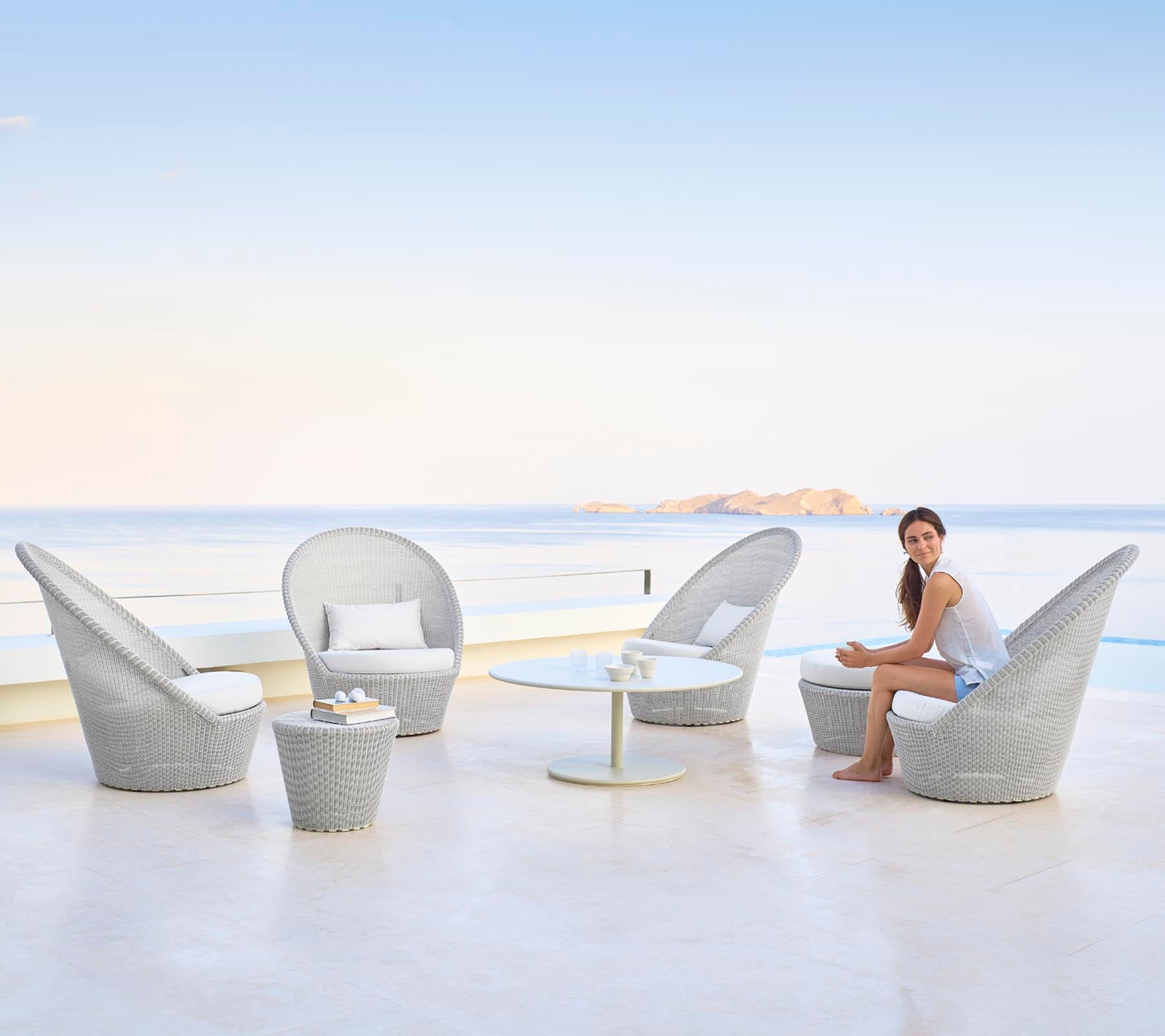 Un arrangement de sièges élégant avec des chaises raffinées et une table, avec une femme assise gracieusement devant un fond d'eau serein.