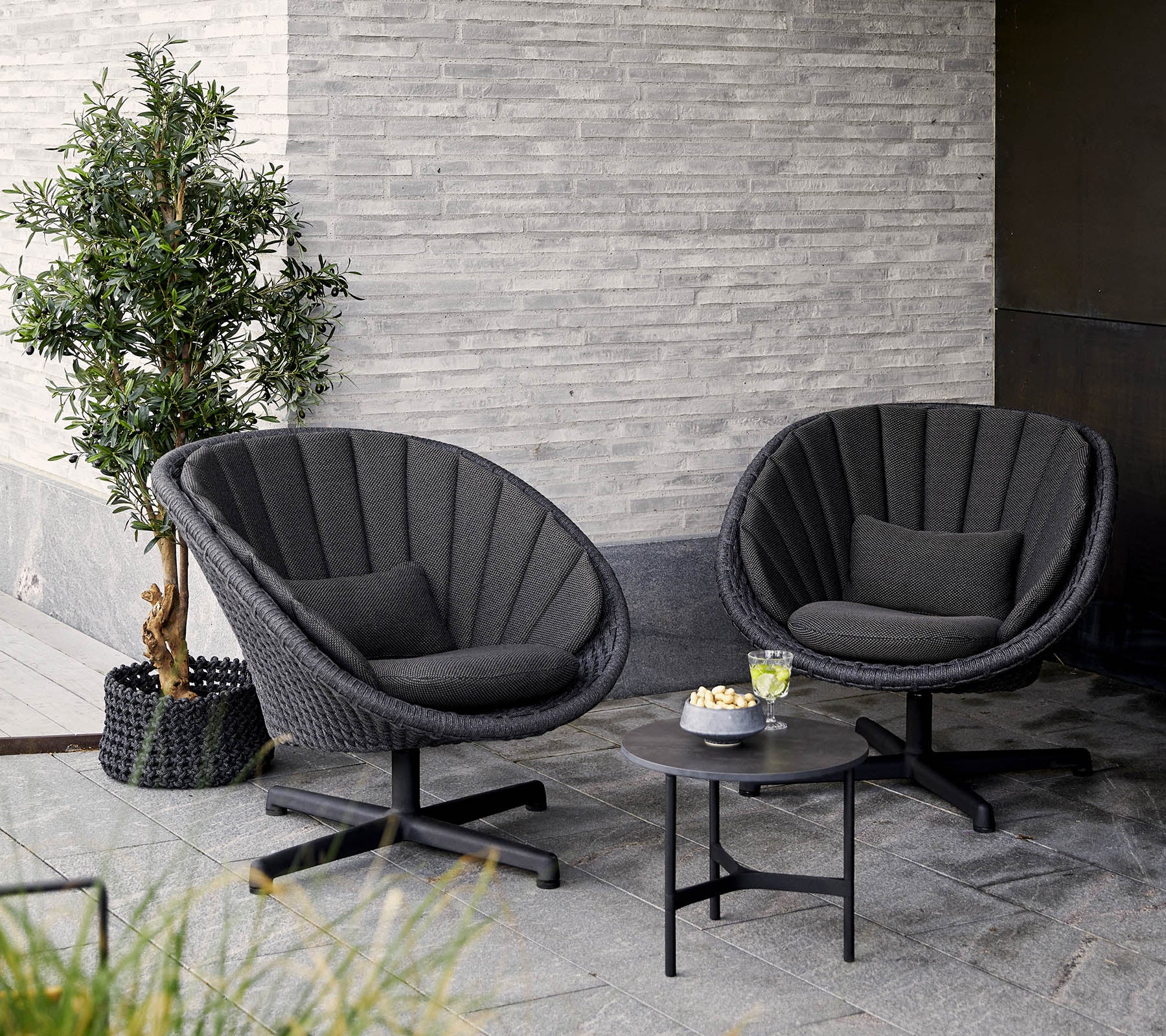 Deux chaises élégantes et modernes au design rond, accompagnées d'une petite table et d'une plante en pot, contre un mur texturé.