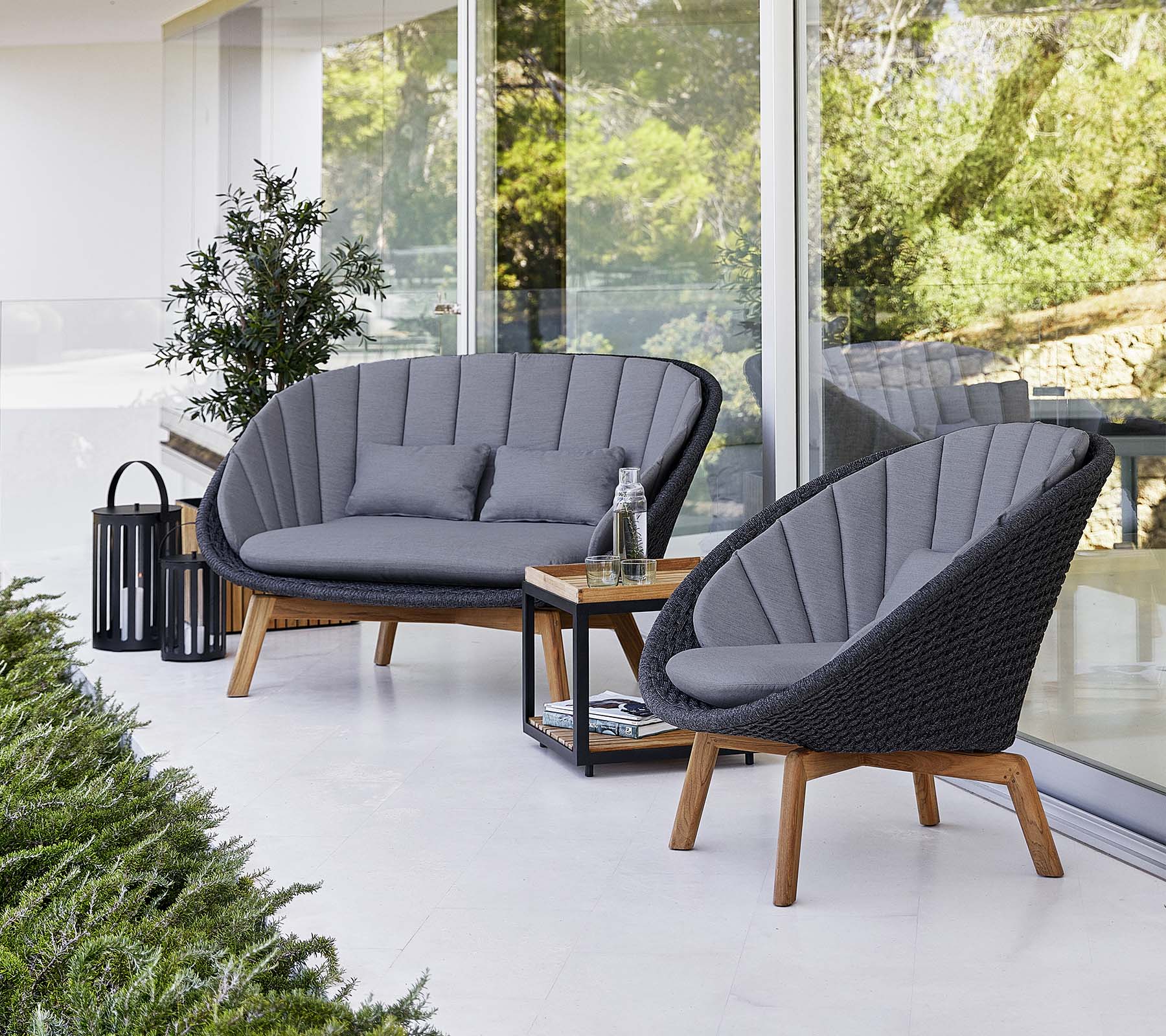 Ensemble de sièges extérieurs élégants avec deux fauteuils rembourrés et un loveseat, accompagné d'une petite table et d'une lanterne décorative.