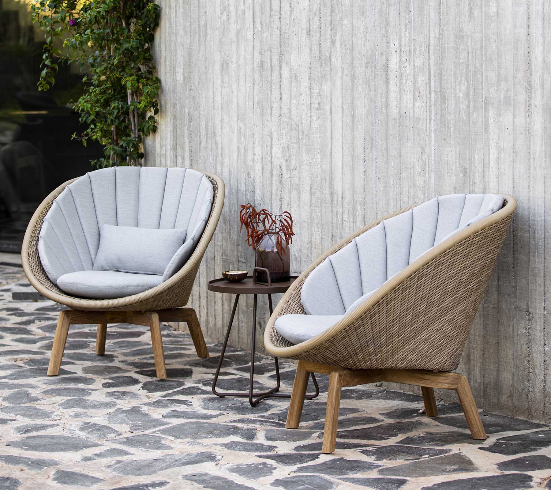 Deux fauteuils élégants et incurvés avec de douces coussins gris à côté d'une petite table ornée d'objets décoratifs, contre un mur texturé.