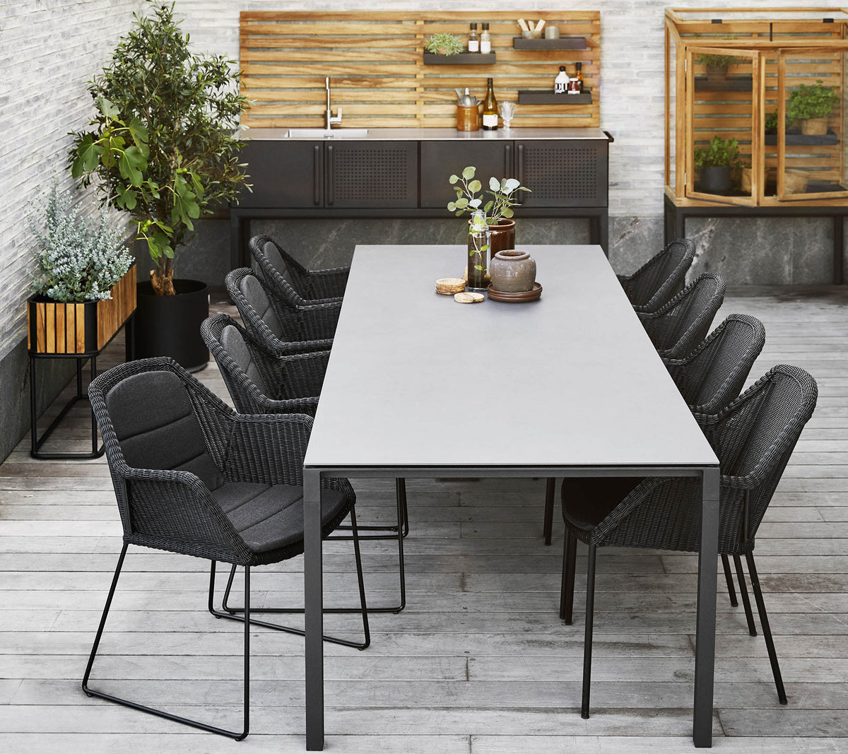 Une installation de salle à manger moderne avec une longue table entourée de chaises noires élégantes, complétée par des plantes décoratives et un fond en bois.