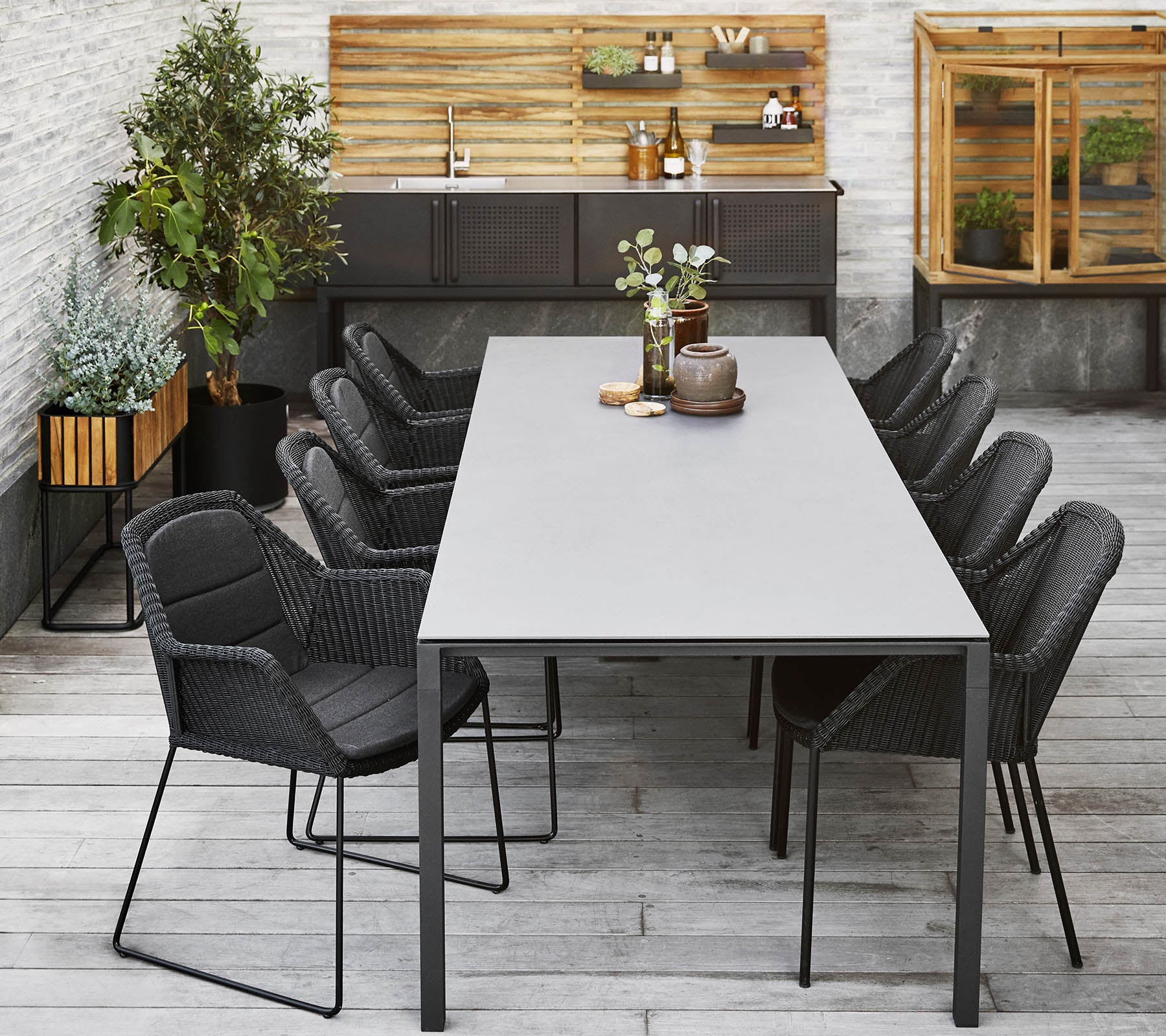 Une installation de salle à manger moderne avec une longue table entourée de chaises noires élégantes, complétée par des plantes décoratives et un fond en bois.