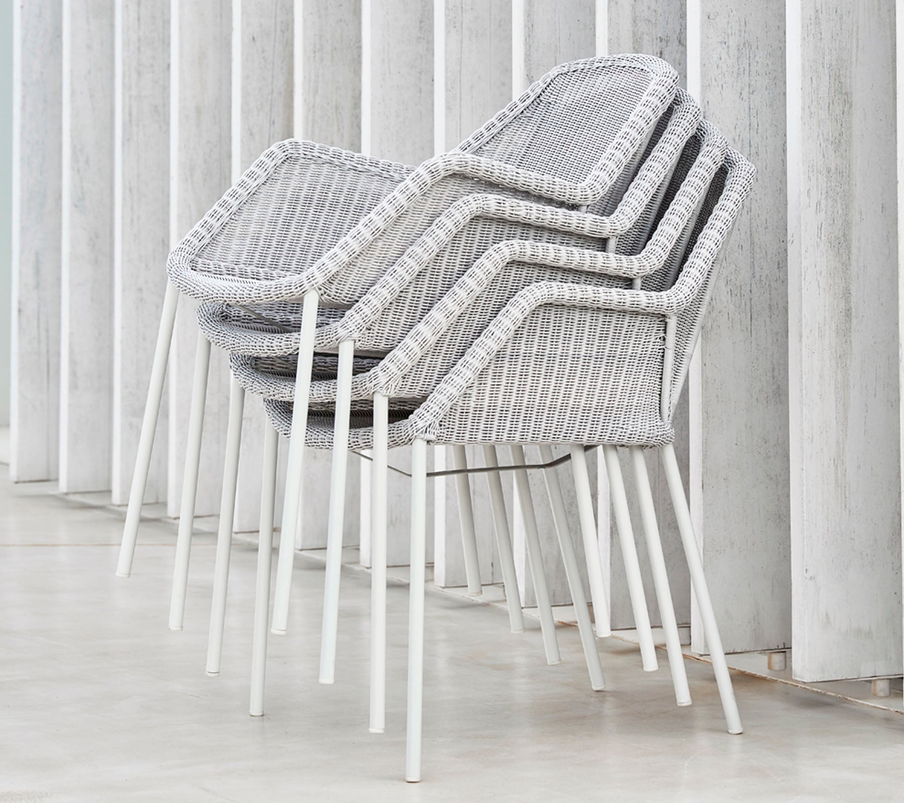 Chaises modernes empilées avec un design tissé en gris et blanc, reposant contre des surfaces verticales, mettant en avant une esthétique épurée et minimaliste.