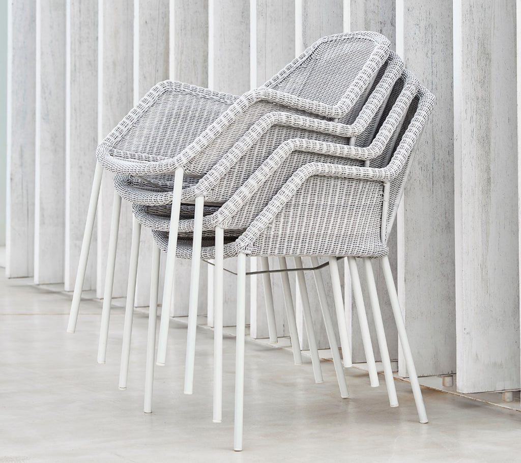 Chaises modernes empilées avec un design tissé en gris et blanc, reposant contre des surfaces verticales, mettant en avant une esthétique épurée et minimaliste.