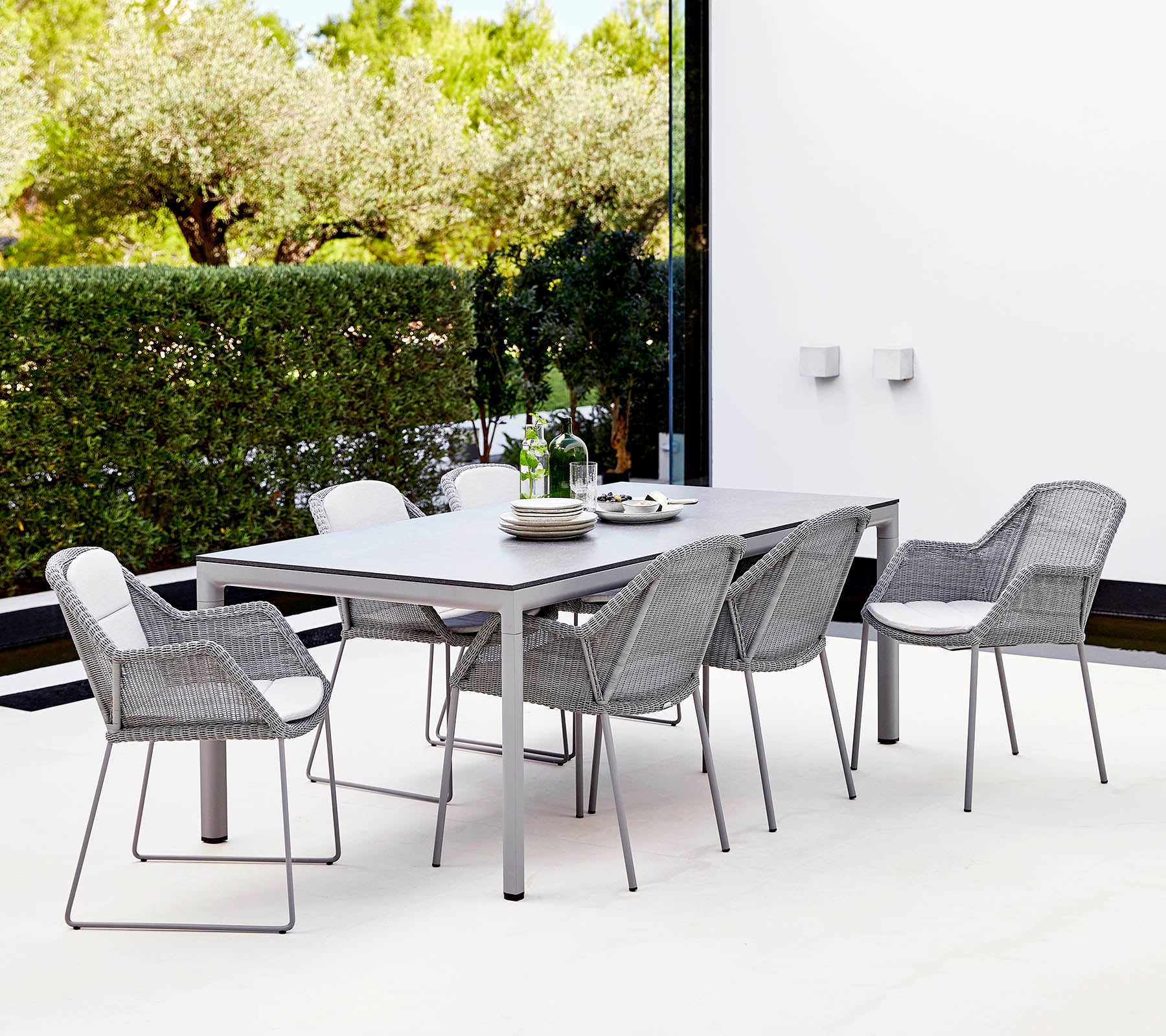 Un ensemble de salle à manger moderne comprenant une table rectangulaire et six chaises tressées élégantes, entourées de verdure.