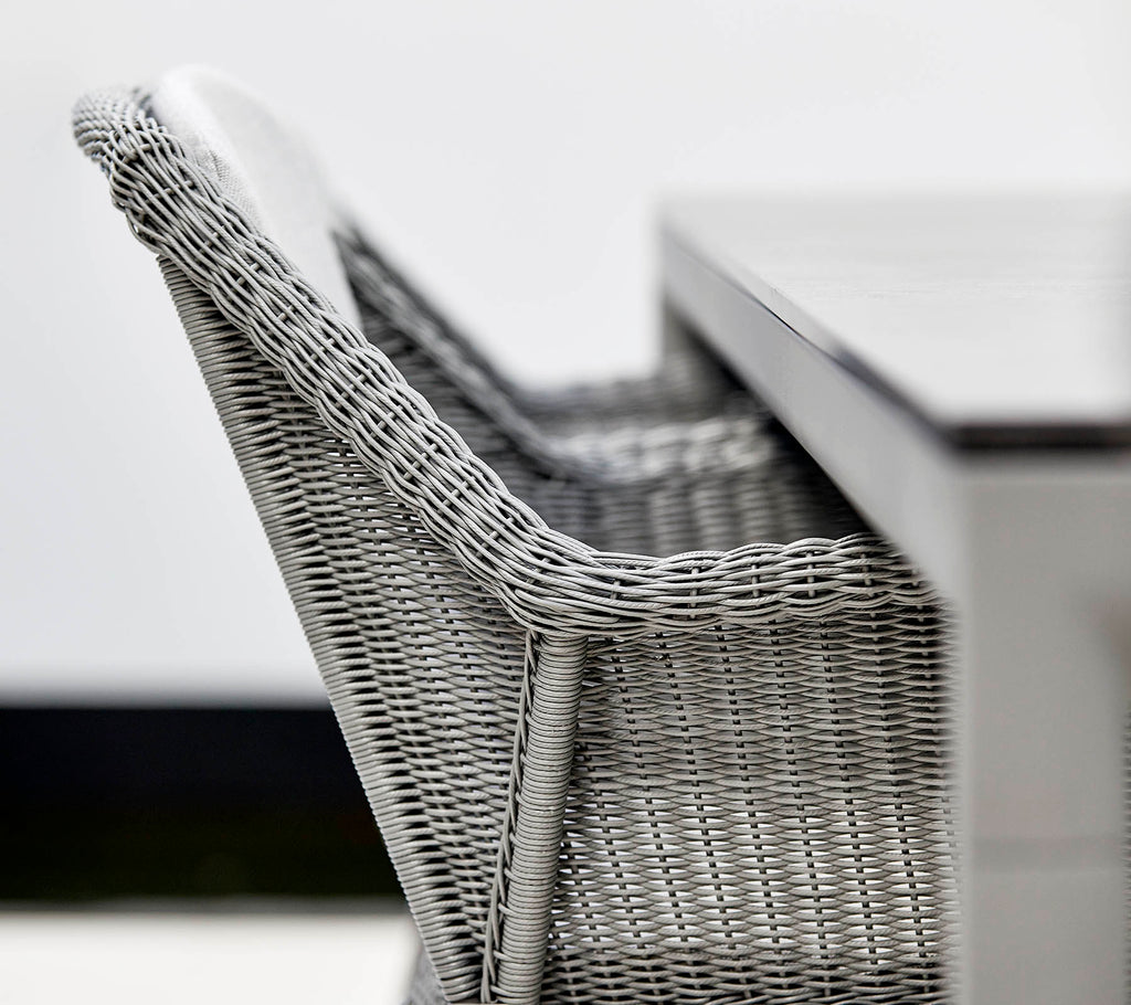 Un gros plan d'une chaise en osier grise élégante à côté d'une table épurée, mettant en avant un design moderne et des textures.