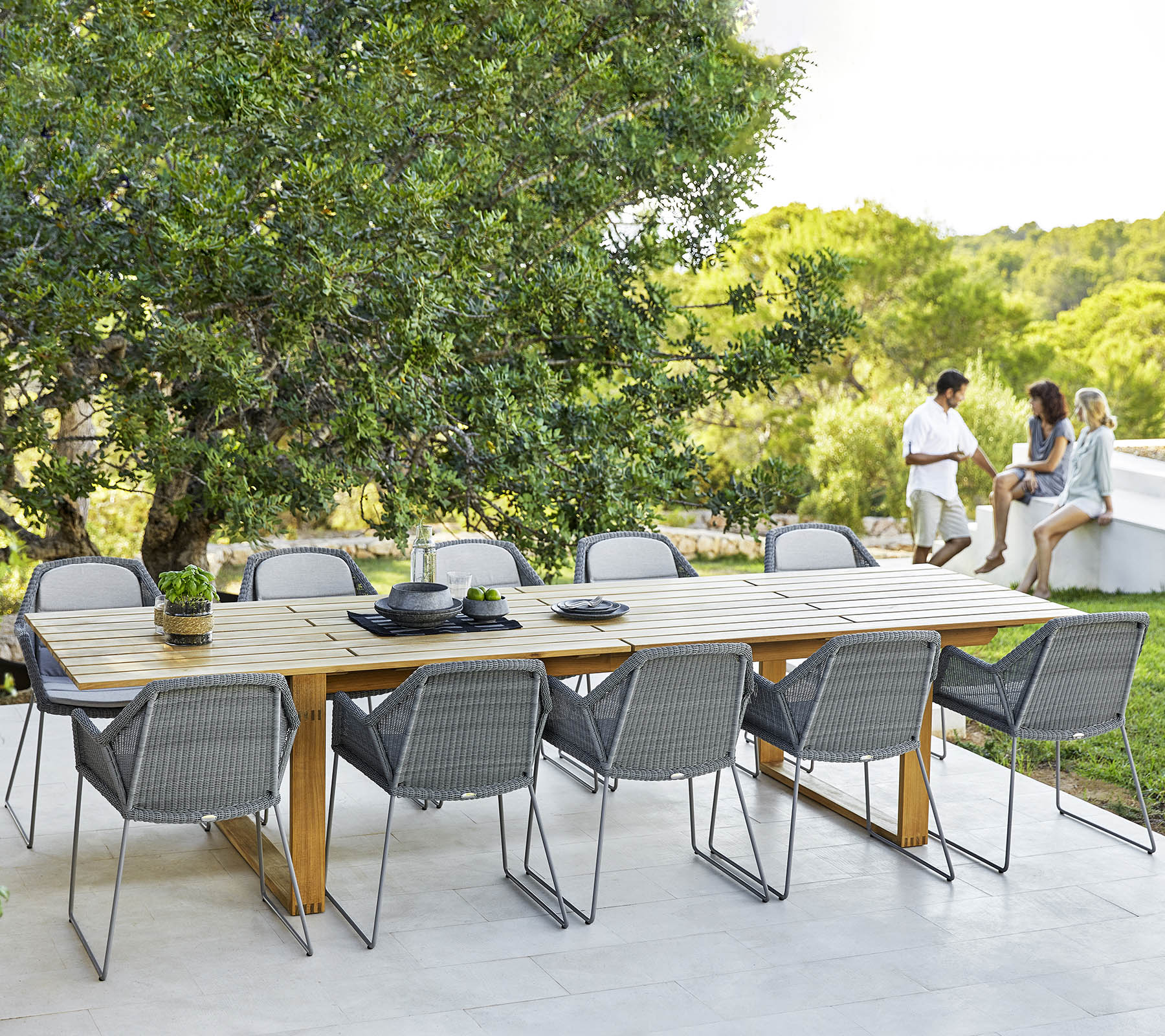Une grande table à manger avec des chaises grises modernes, dressée pour un repas, entourée de verdure et d'une atmosphère relaxante.