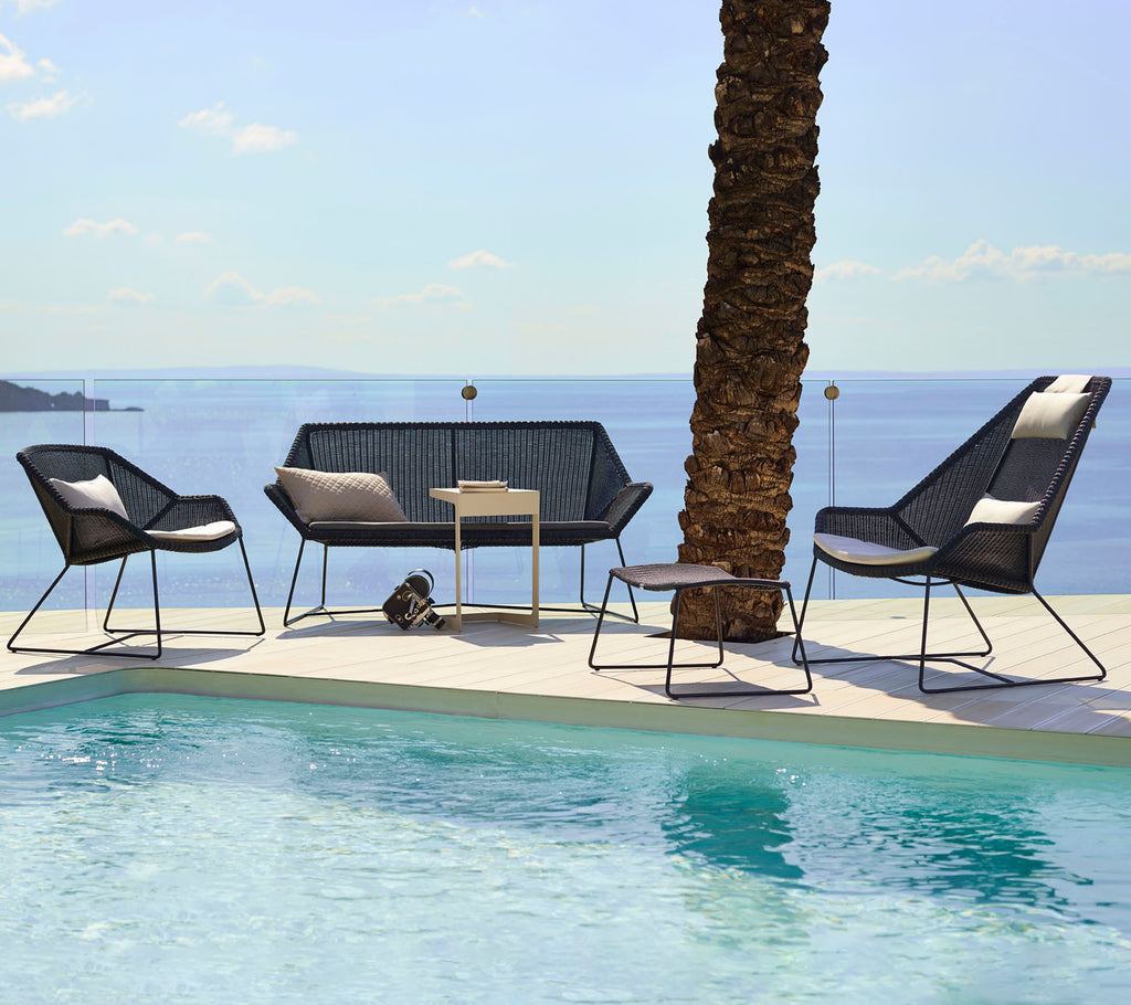 Des sièges modernes dans le lounge avec des chaises noires et un loveseat à côté d'une piscine.
