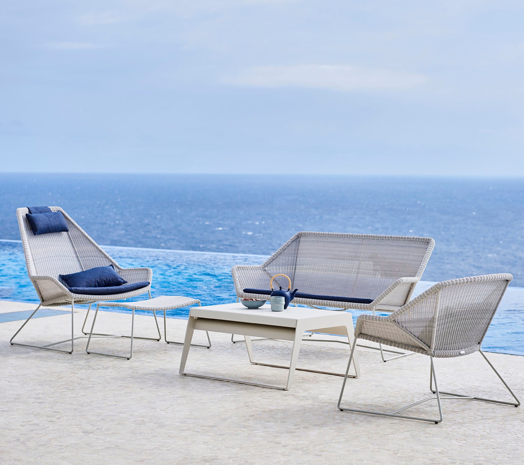 Ensemble de meubles d'extérieur modernes comprenant des chaises élégantes et une table, sur fond d'eau et de ciel.