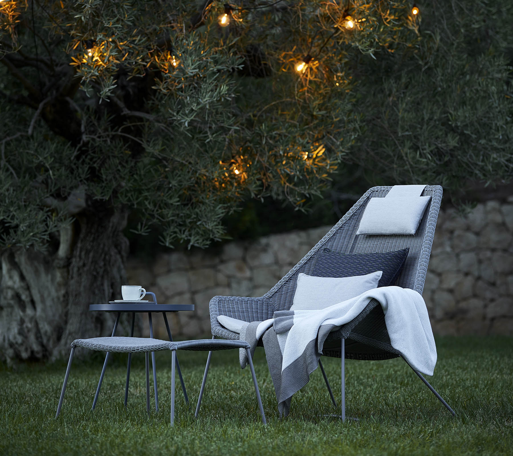 Agencement de sièges élégant avec un fauteuil confortable, un doux plaid et une table d'appoint, éclairé par des lumières douces en arrière-plan.