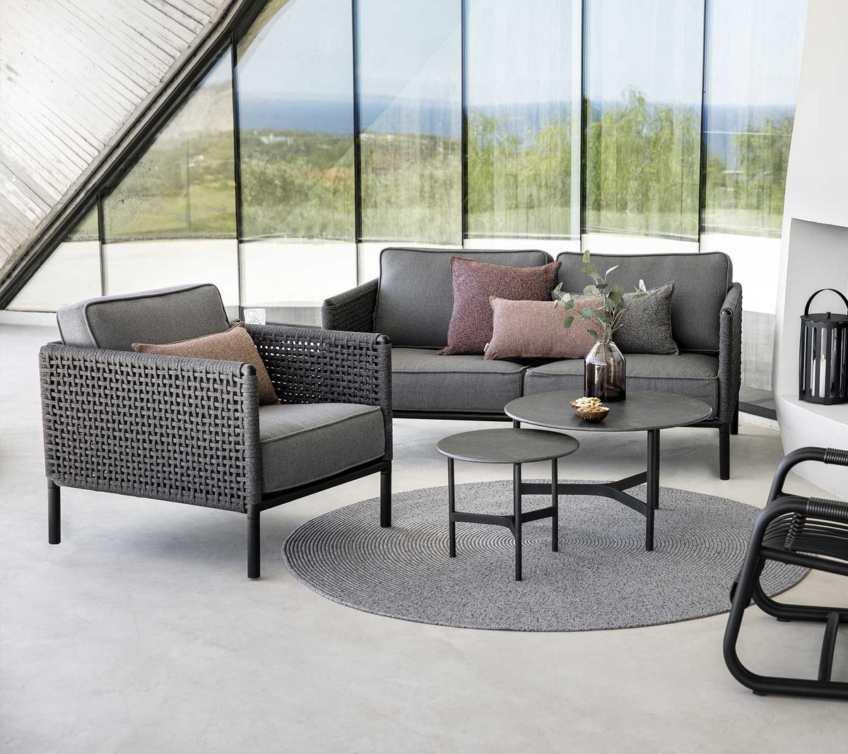Agencement de sièges stylé avec un canapé gris et un fauteuil avec des coussins, accompagné d'une table ronde sur un tapis texturé.