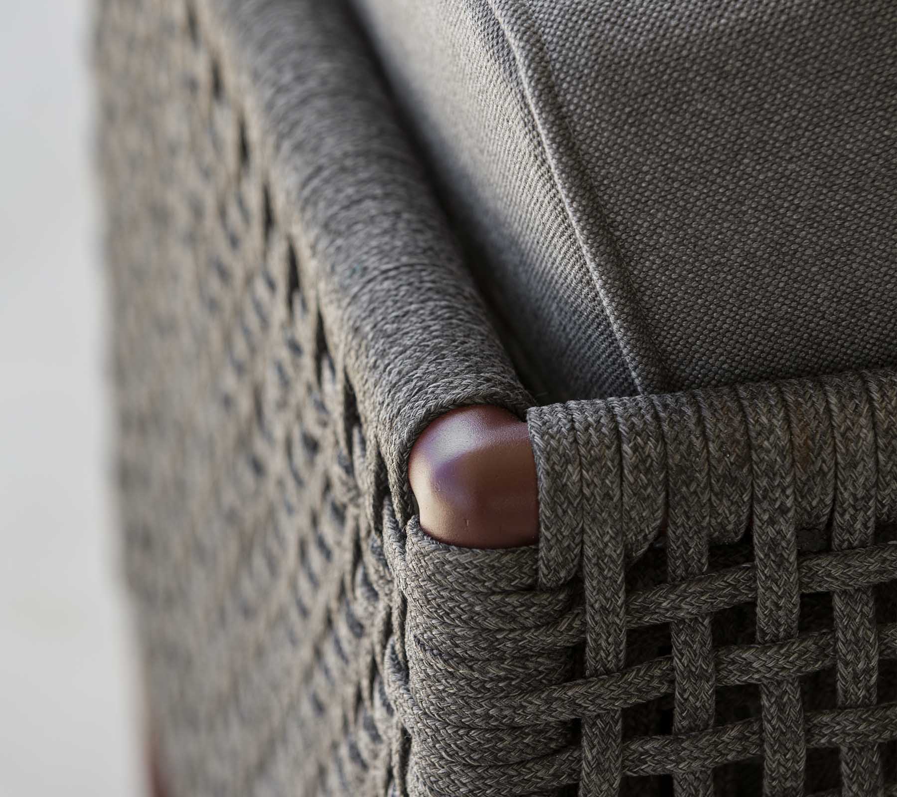 Gros plan d'un coin de meuble tissé avec un élégant tissu gris et des accents en bois lisses, mettant en valeur un mélange de textures et de styles.