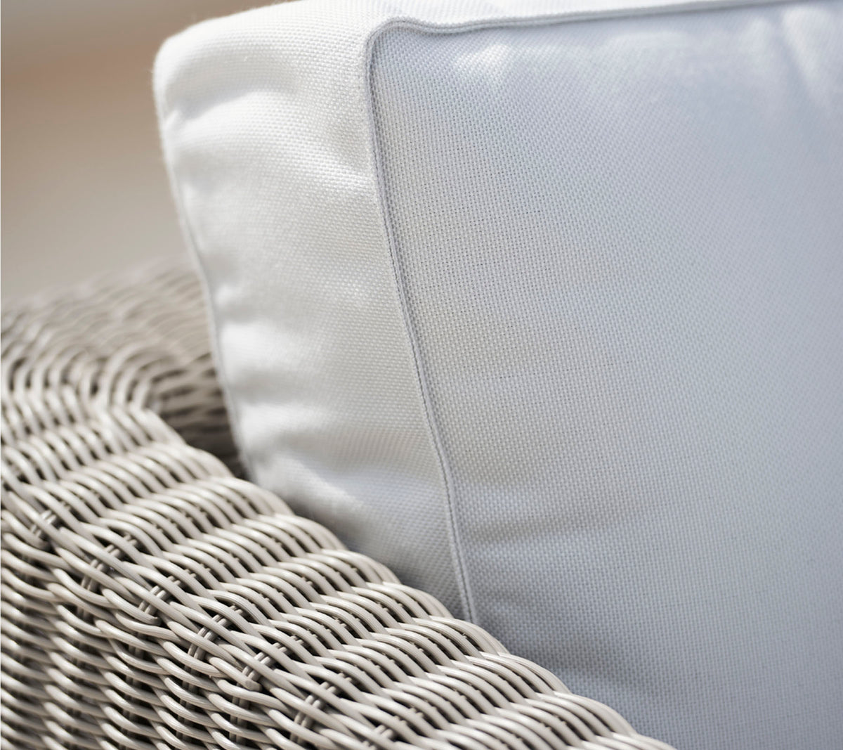 Gros plan d'une chaise en osier avec un coussin blanc, mettant en valeur la texture de l'osier et le tissu lisse du coussin.