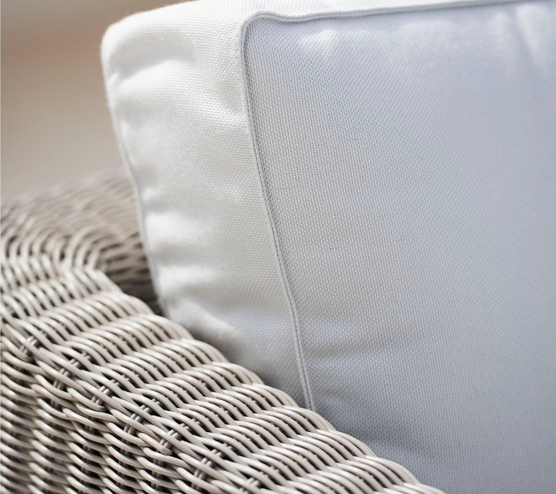 Gros plan d'une chaise en osier avec un coussin blanc, mettant en valeur la texture de l'osier et le tissu lisse du coussin.
