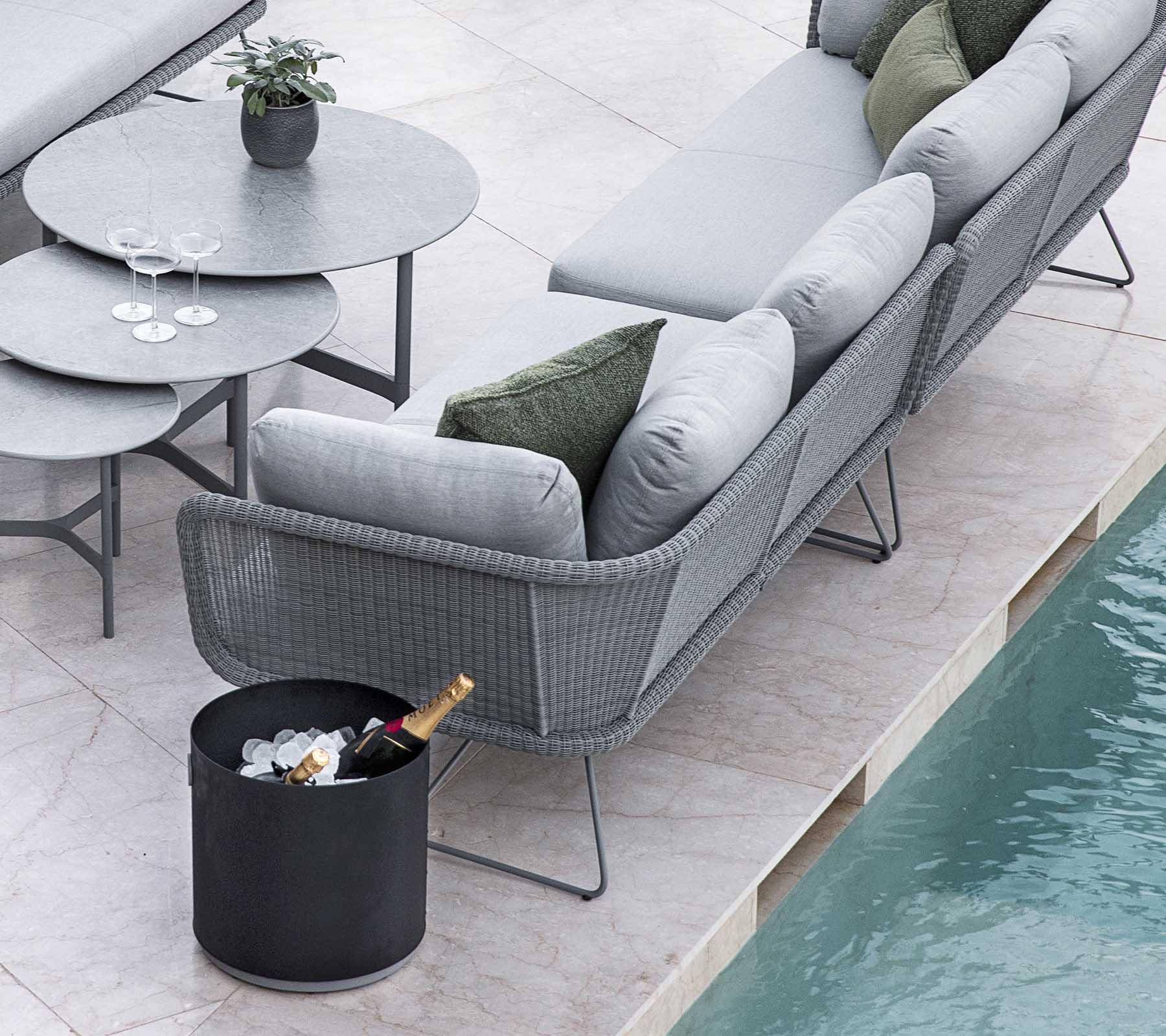 Arrangement moderne de sièges extérieurs avec un canapé gris élégante et une table ronde, agrémenté d'un seau de glace et de boissons.