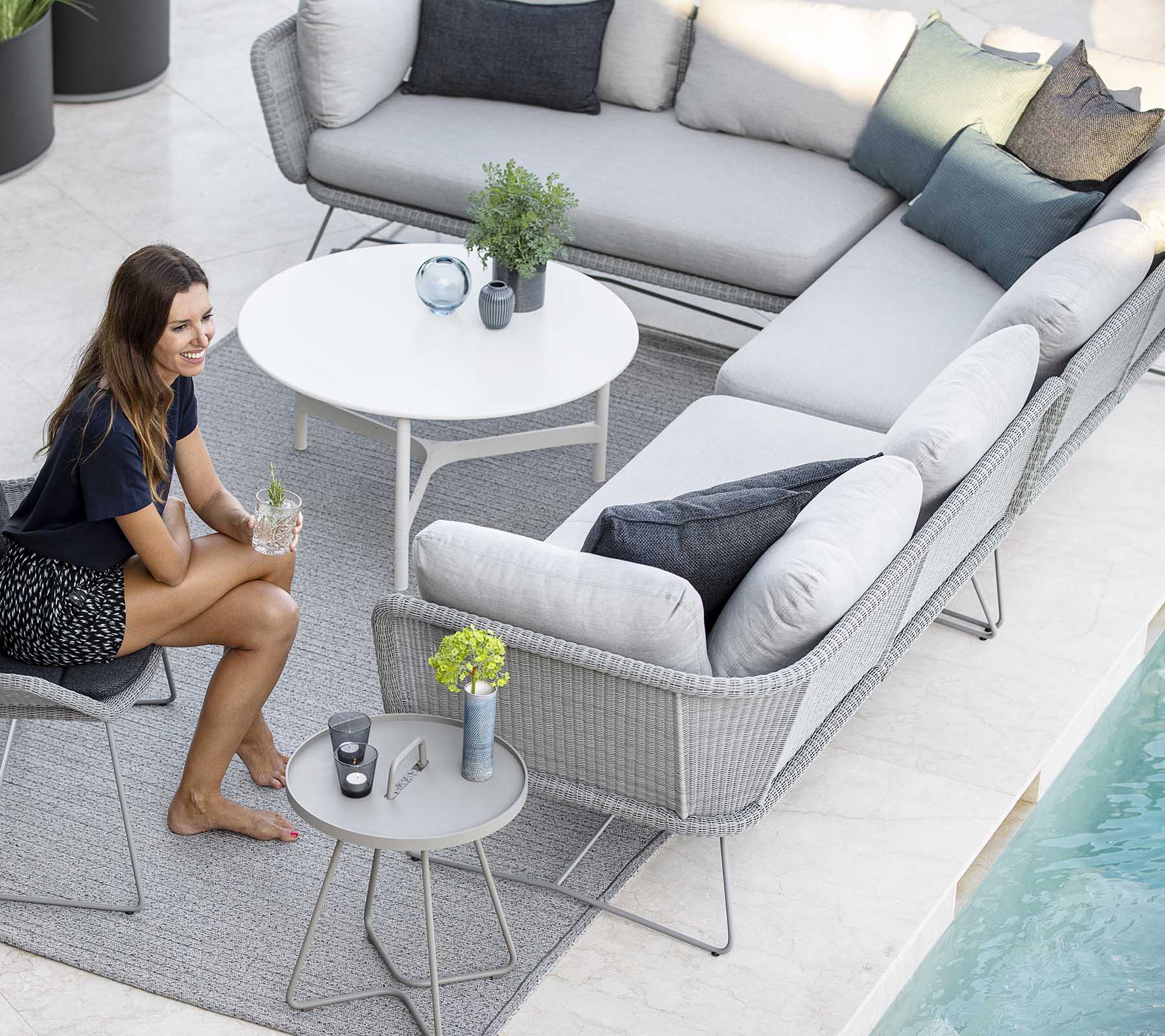 Un aménagement de sièges d'extérieur élégant avec un canapé, des coussins décoratifs et une petite table, complété par des plantes et une piscine à proximité.