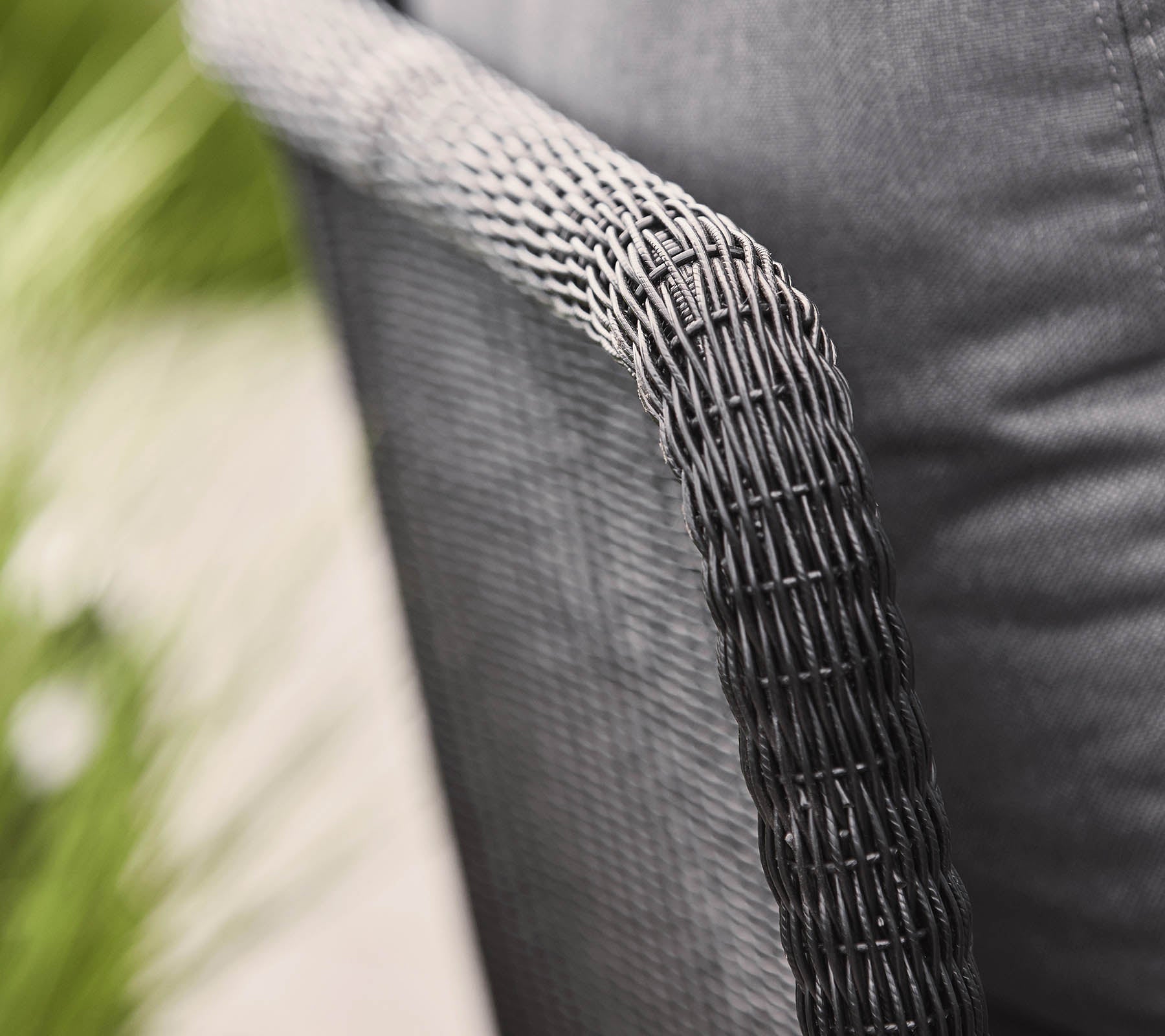 Gros plan d'un bras de chaise tissé avec une finition noire texturée, mettant en avant un design moderne et un siège en tissu confortable.