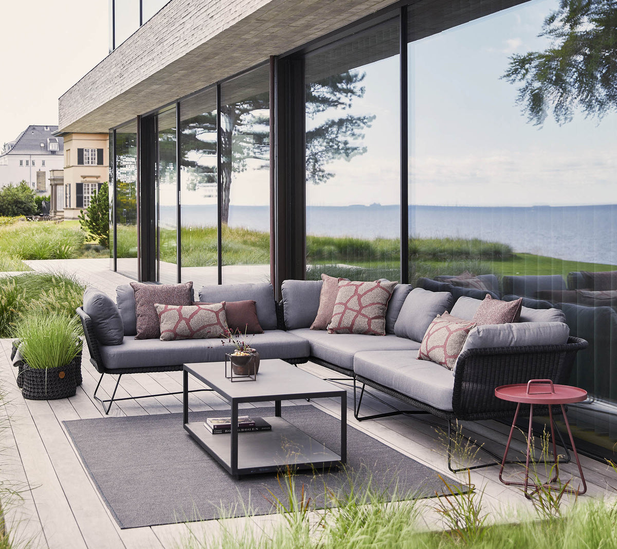 Espace extérieur moderne avec un canapé d'angle avec des coussins, une table basse et des éléments décoratifs au milieu d'une végétation luxuriante.