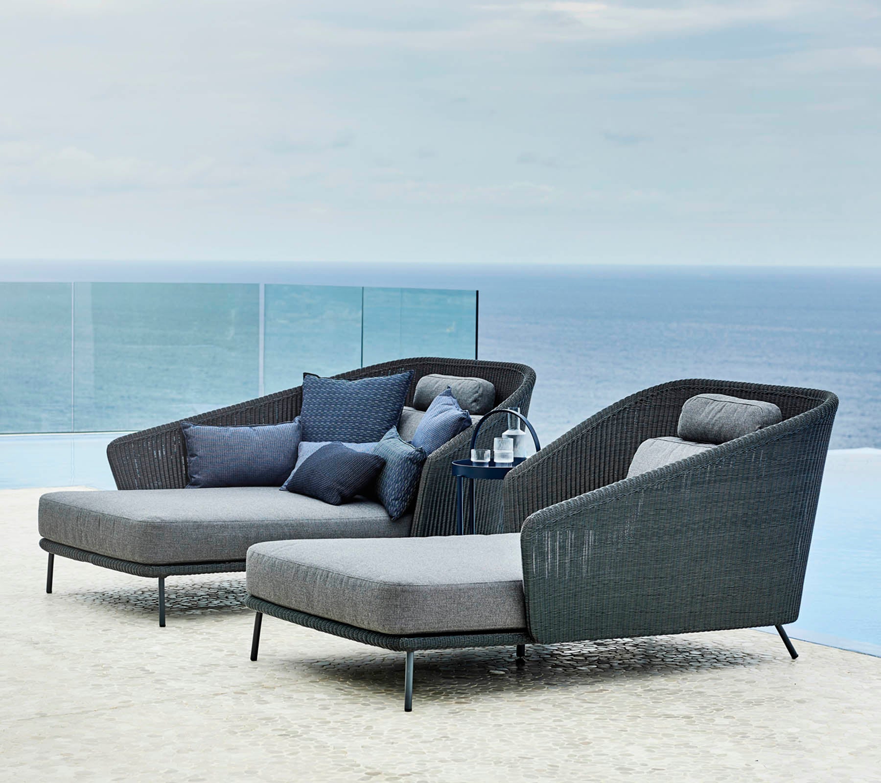 Deux fauteuils lounge élégants avec des coussins et une petite table d'appoint, surplombant une vue sereine sur l'océan.