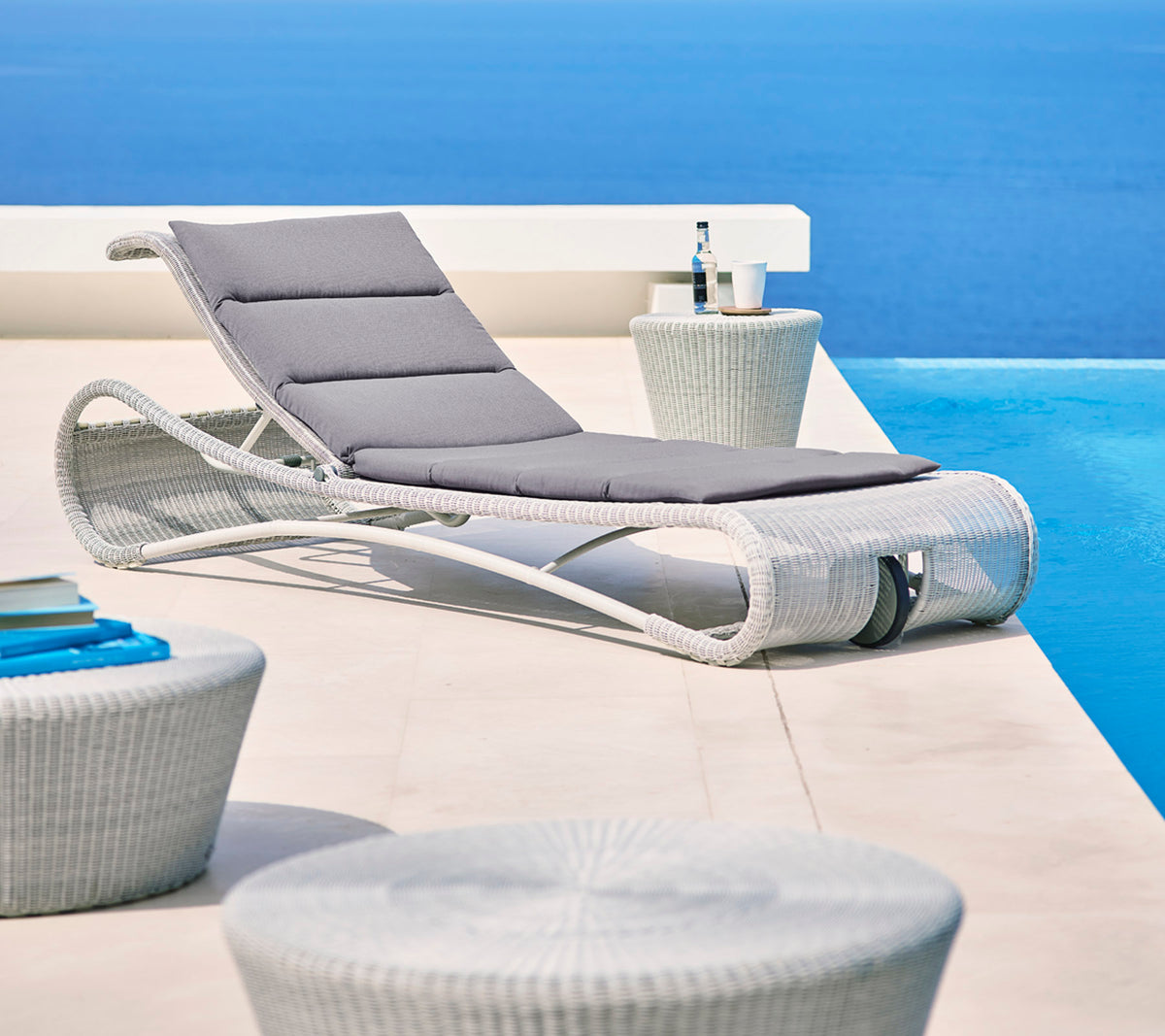 Chaise longue élégante avec coussin gris à côté de tables d'appoint modernes, sur fond bleu serein. Parfaite pour se détendre.